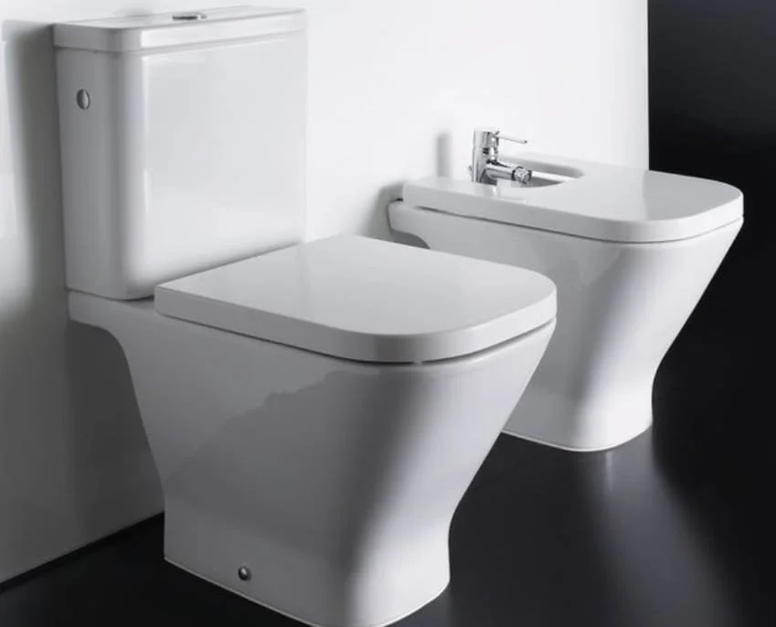 Inodoro y bidé blancos en un baño con paredes blancas y piso negro.