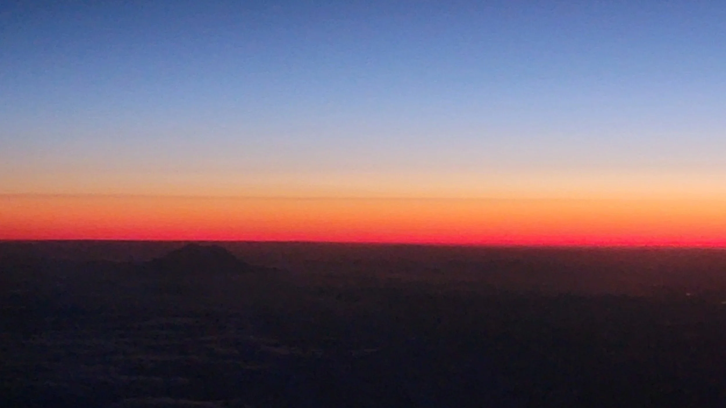 Photo of a sunset with a colorful sky transitioning from orange to blue and dark silhouettes of mountains in the foreground.