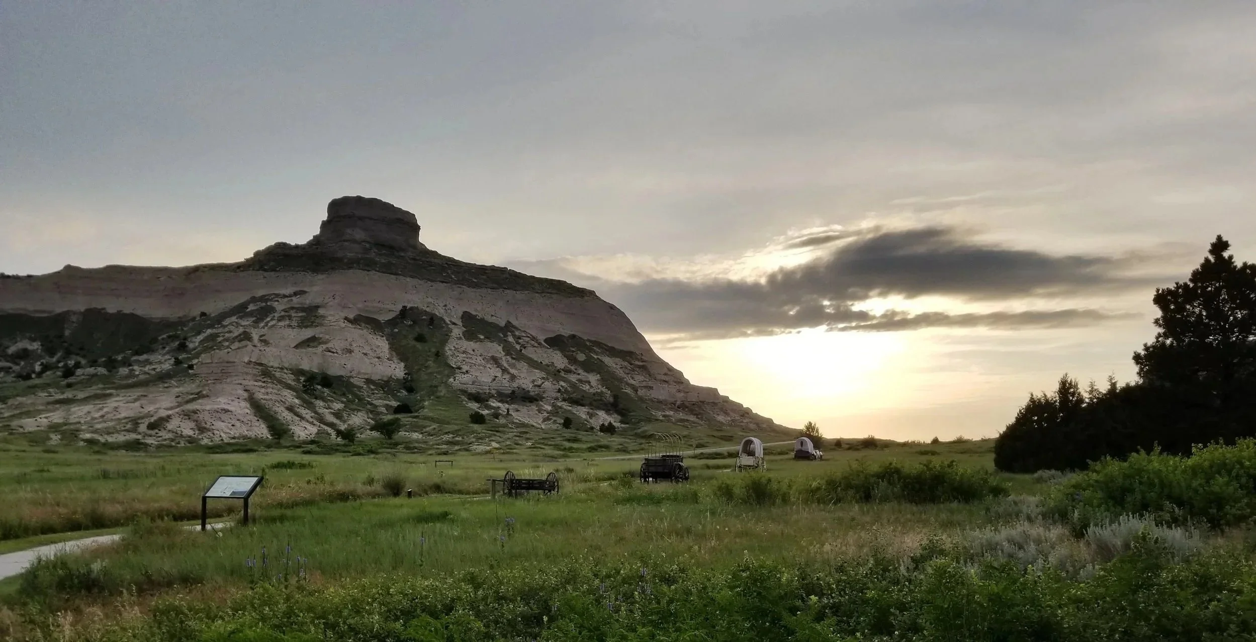 Sunset over bright green plains in summertime, with gray skies overhead.