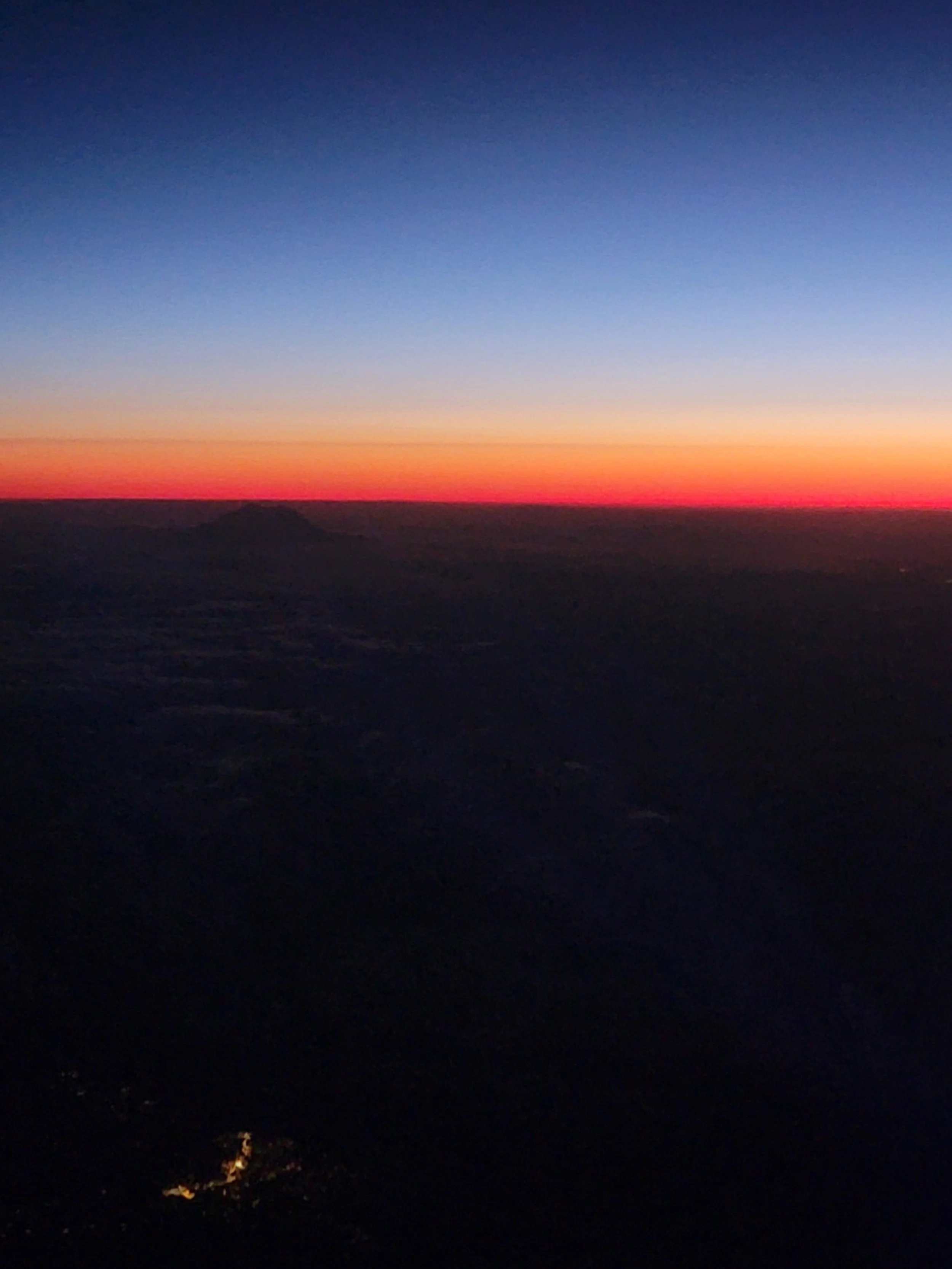 Sunset or sunrise sky with a gradient of colors from deep blue to orange and pink, over a dark landscape.