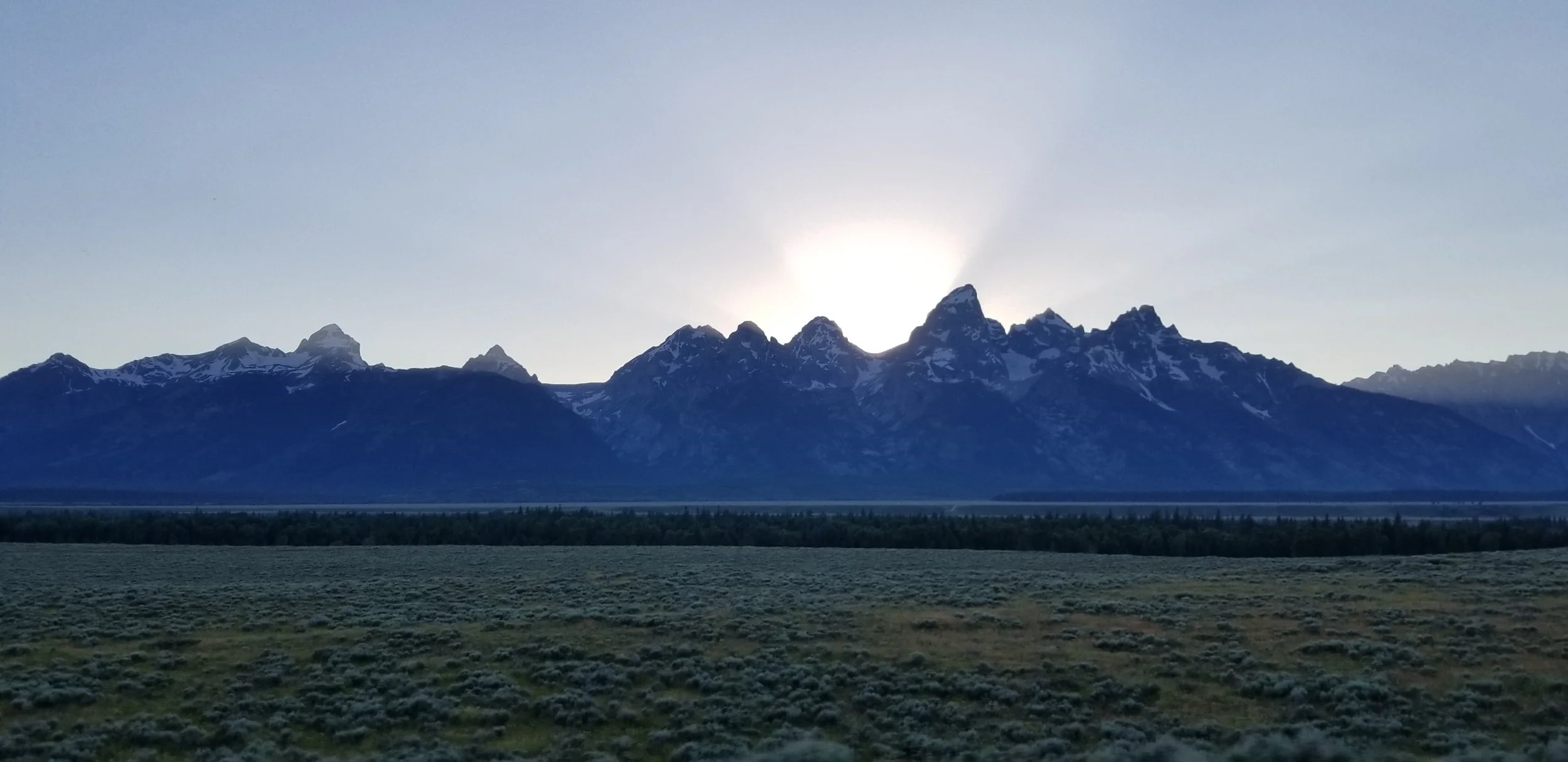 Sunset between the peaks of a mountain range, overlooking an open expanse.
