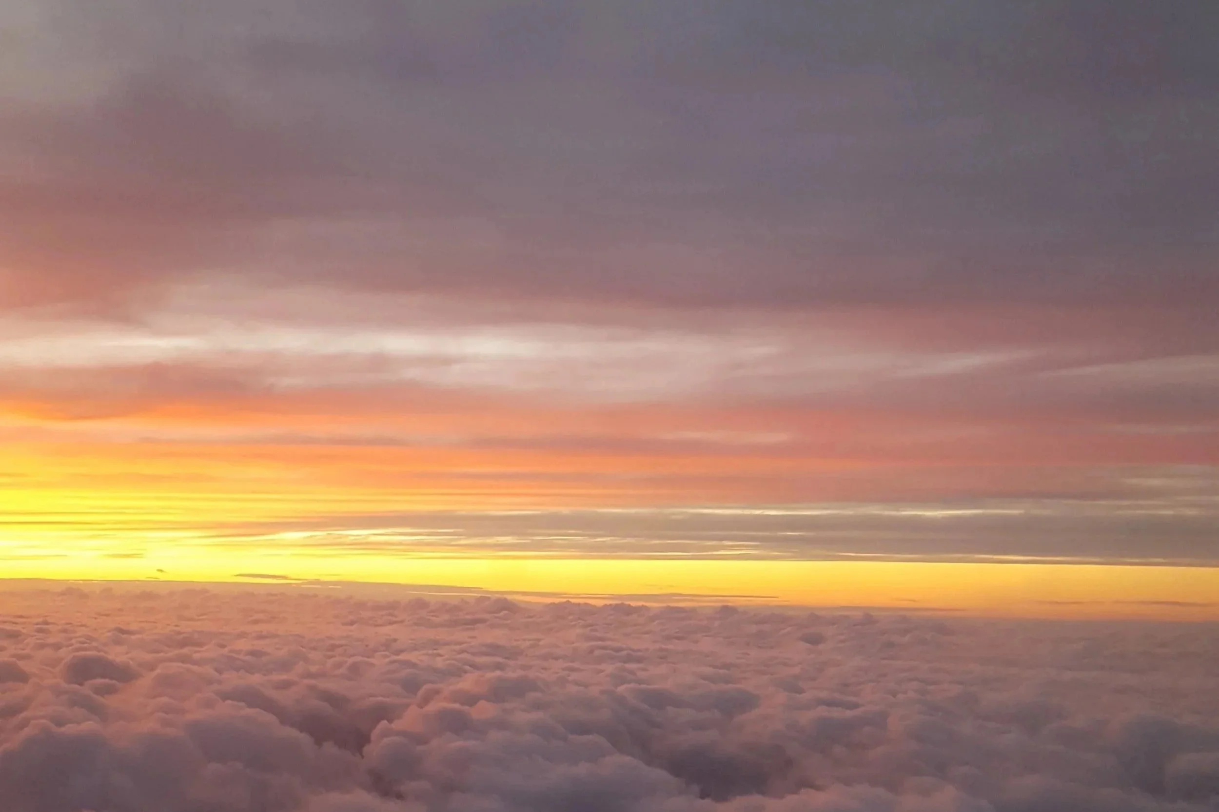 View of colorful sunset above the clouds with shades of orange, pink, purple, and yellow in the sky.