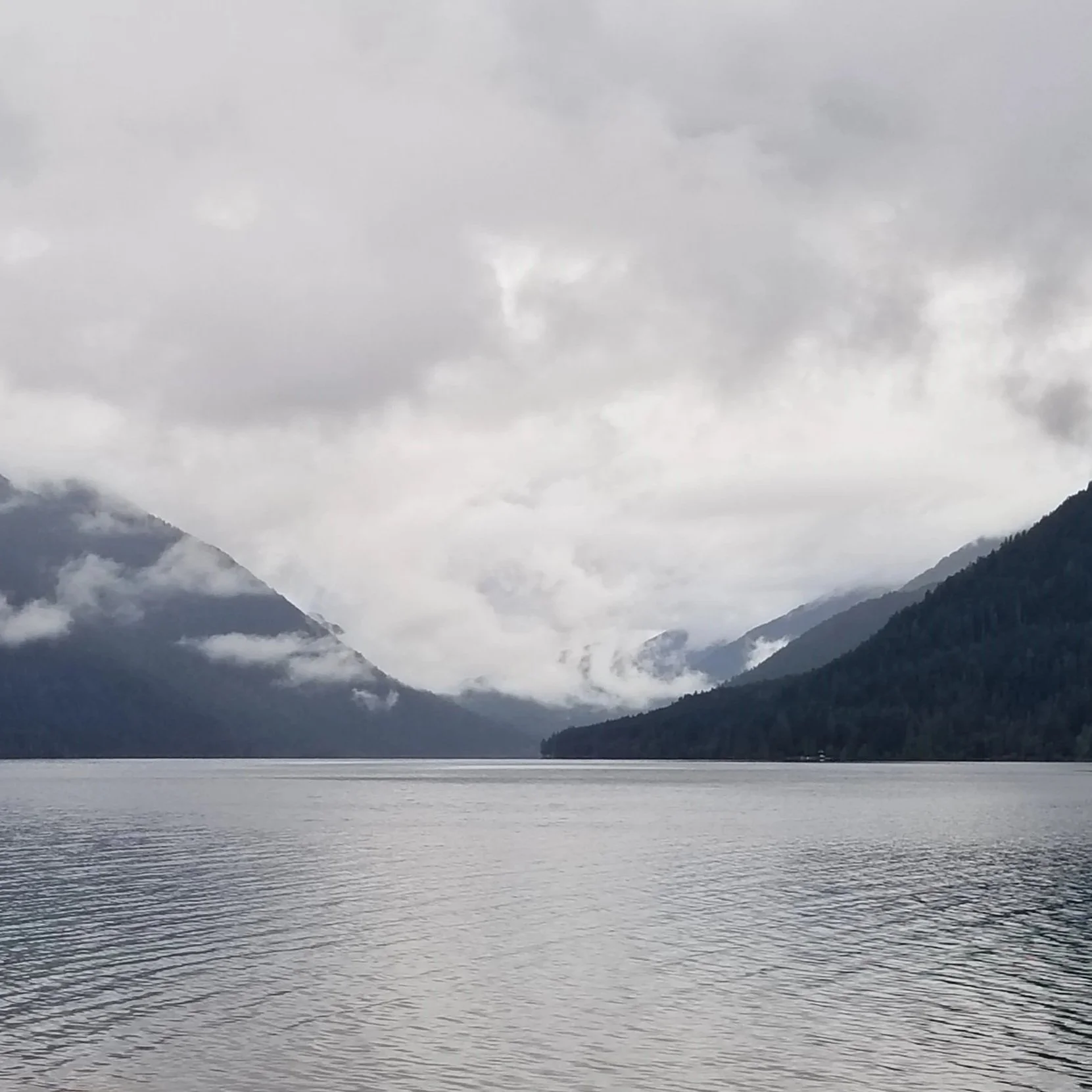 A dense fog gathers between mountain ranges above a crystal clear lake. The entire scene has the color of ice.