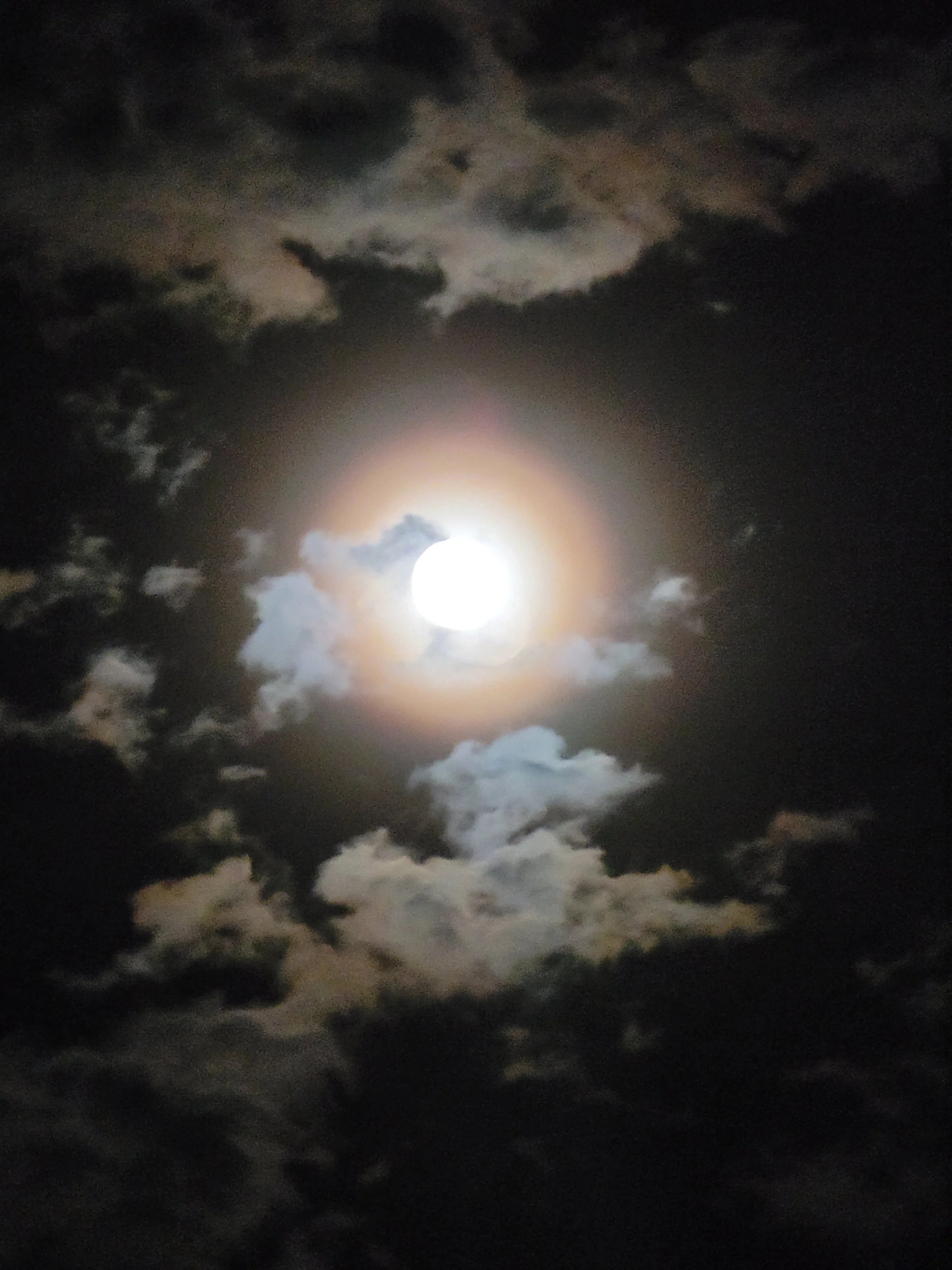 The full moon shining brightly in the night sky surrounded by dark clouds.