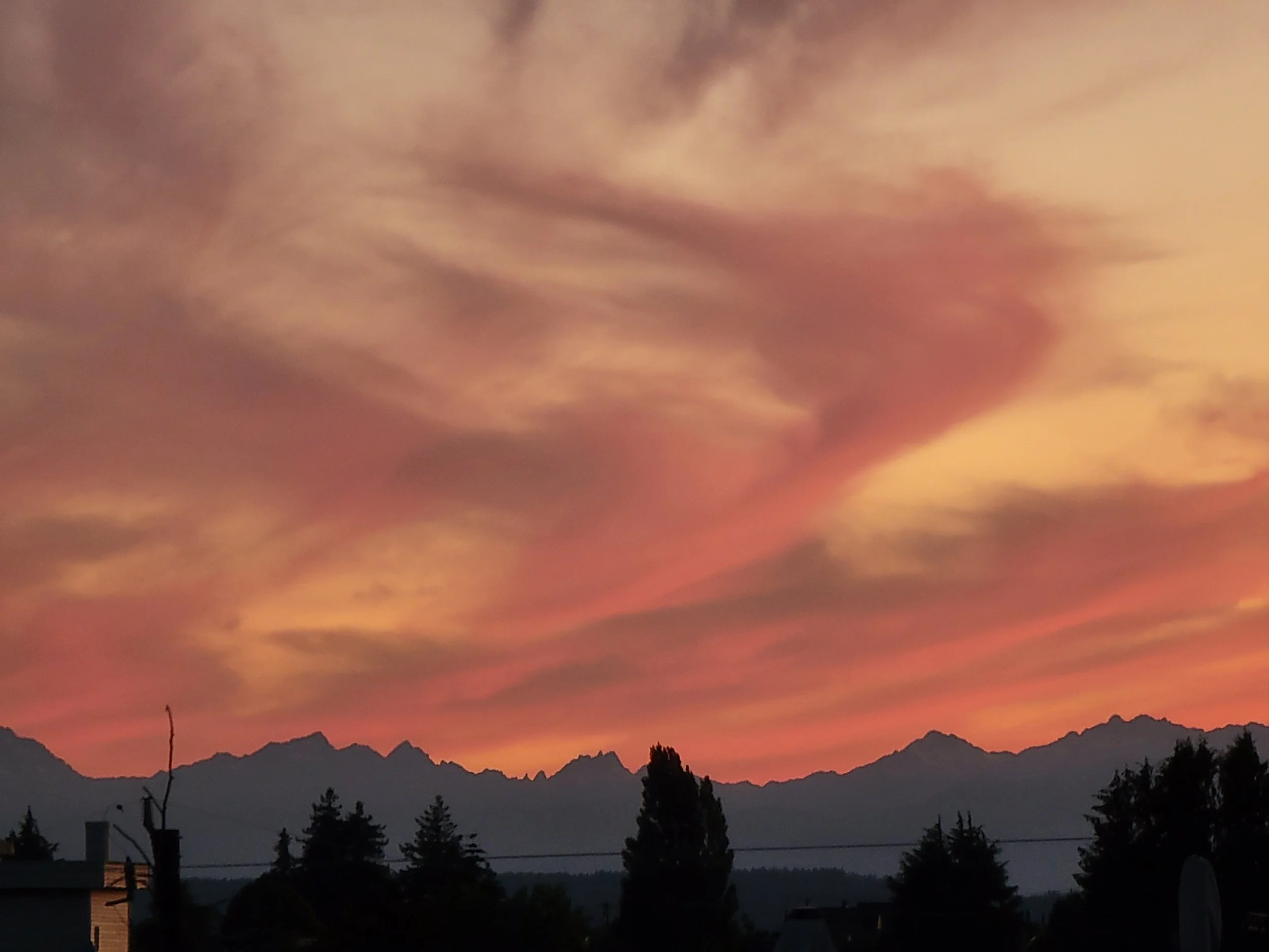 A colorful sunset sky with pink and orange clouds over a silhouette of mountain range and trees in the foreground.