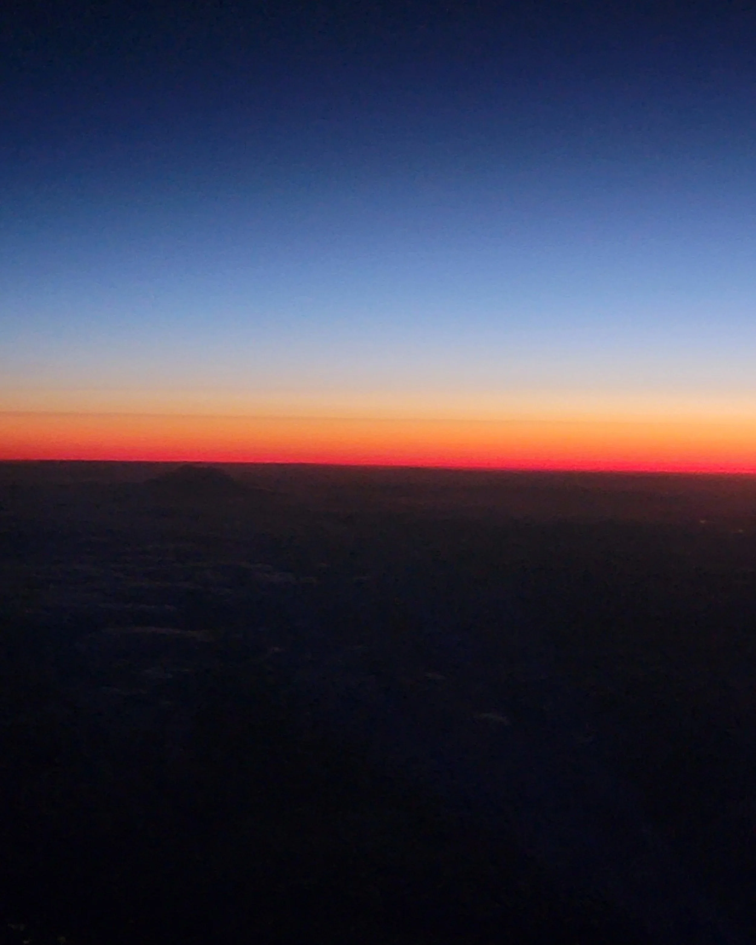 A sunset over a dark horizon with a colorful sky transitioning from dark blue to orange and pink hues.