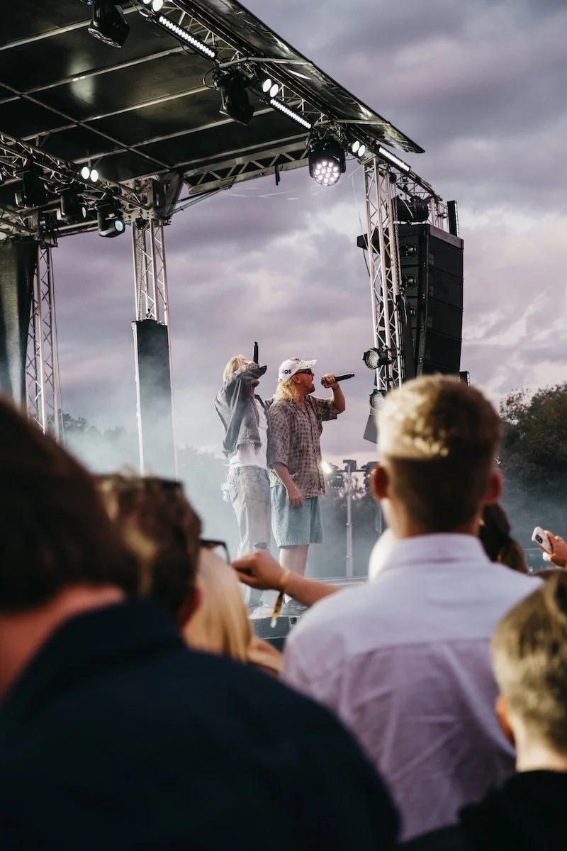 En utomhuskonsert med flera personer på scen under en mörk himmel, med publik i förgrunden.