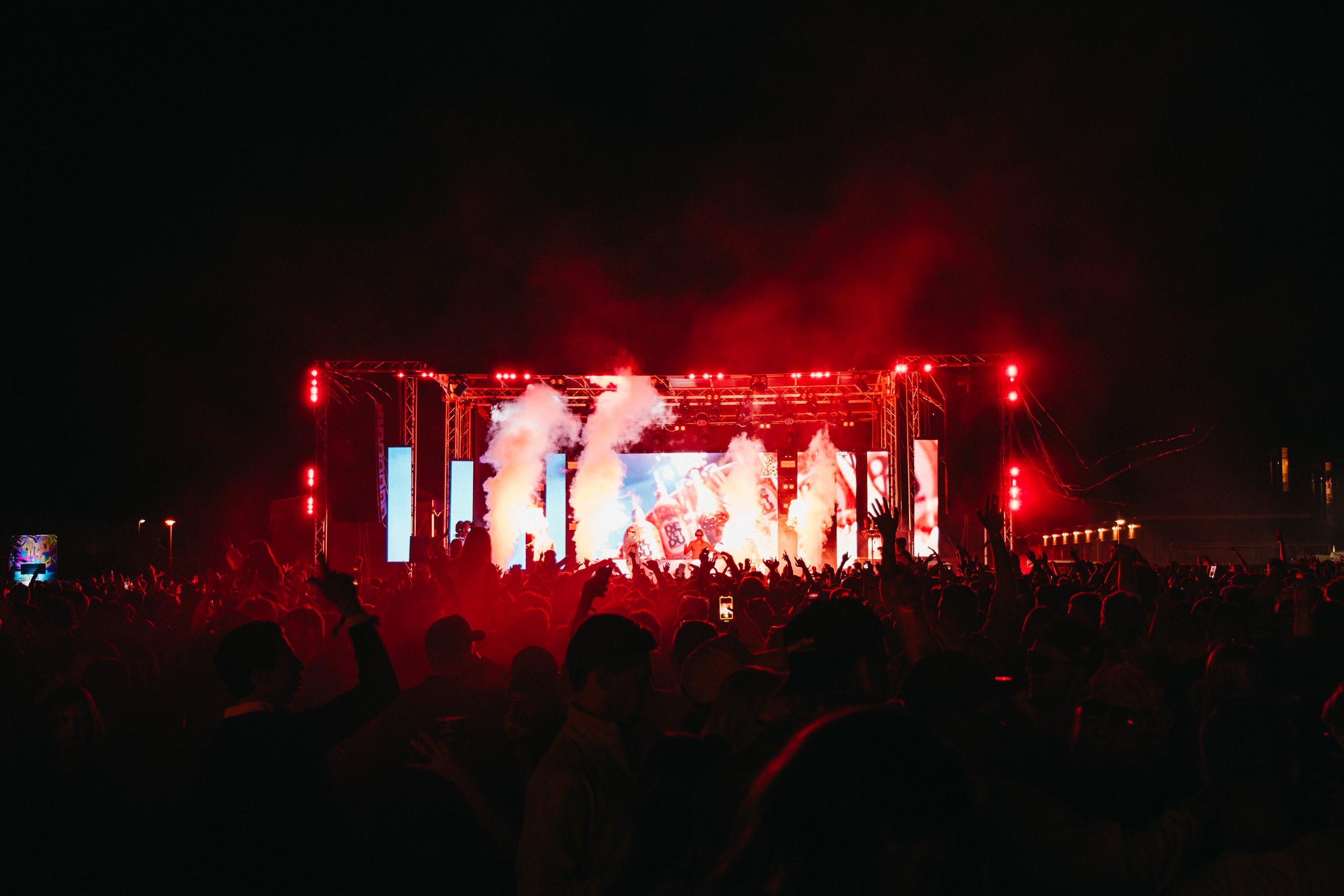 En stor utomhuskonsert på natten med en fullsatt publik som tittar på en scen med ljus och rök.