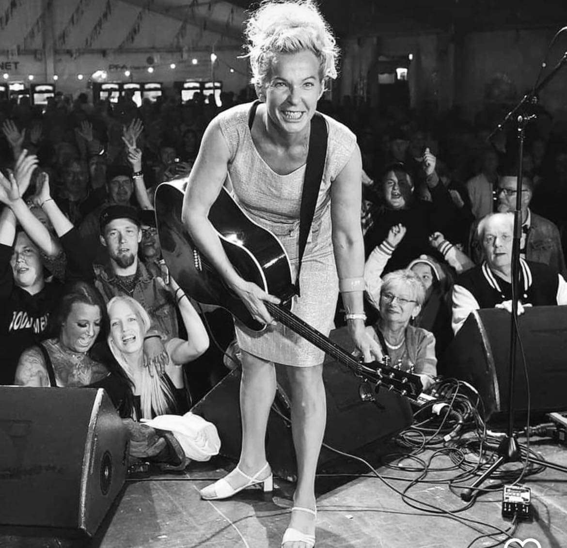 En kvinna spelar gitarr på scenen inför publik som visar entusiasm och glädje.