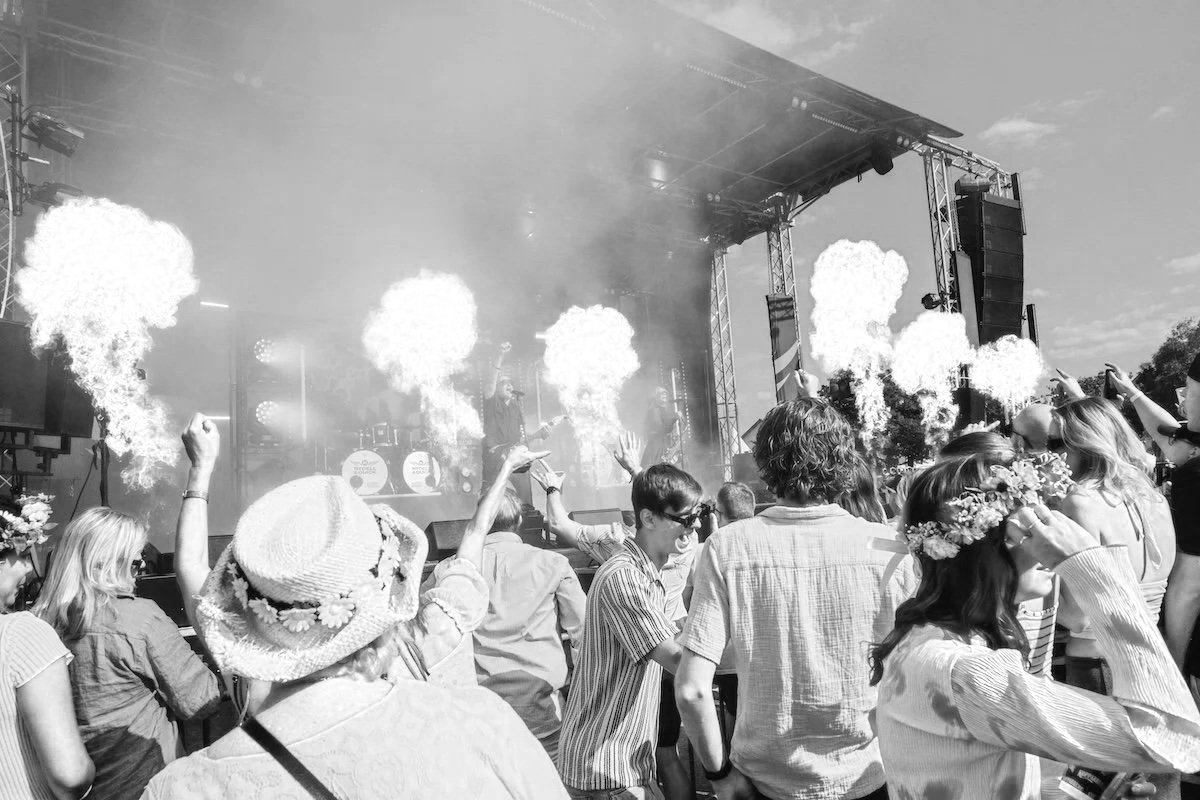 Folk samlat framför en scen som framträder i svartvitt, med eld- och pyroteknik som skjuts ut i luften under en konsert.