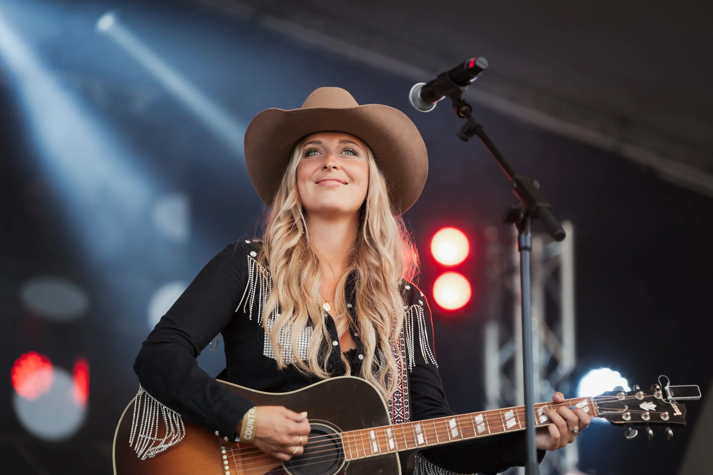 Kvinna i cowboyhatt spelar akustisk gitarr på scen under konsert.