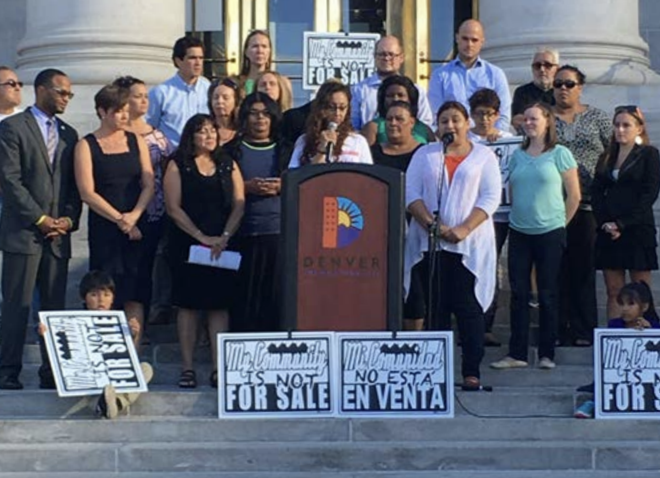 A group of people at a podium with signs that say Our community is not for sale