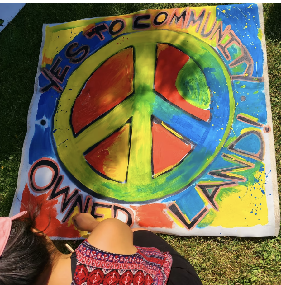 A peace sign painting with the words "Yes to Community Owned Land"