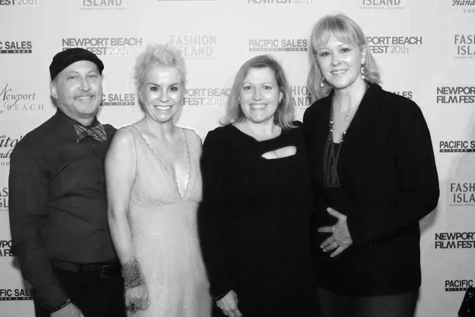 Four people smiling at a fashion event with a backdrop featuring event logos and names.