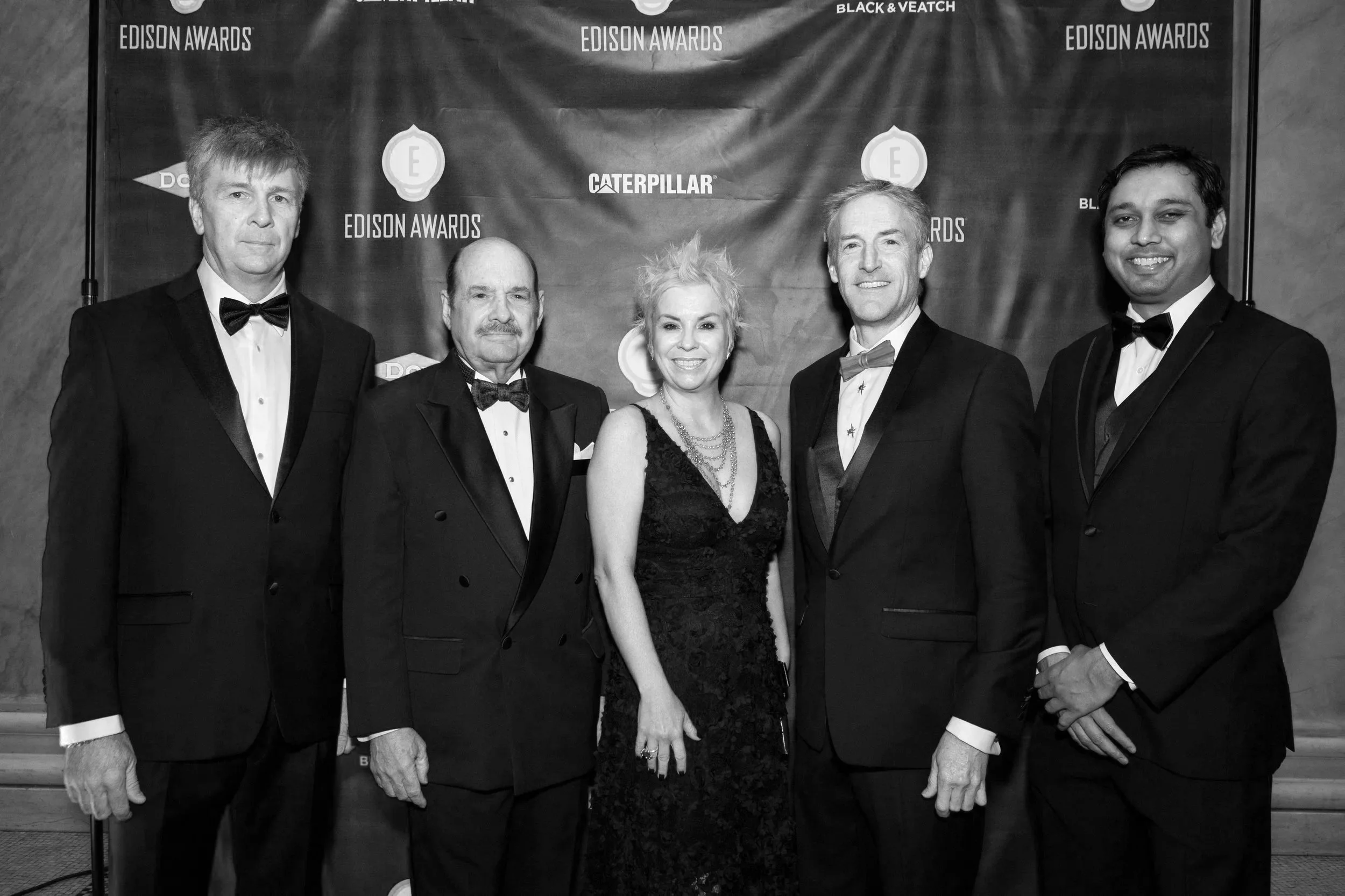 Group of five people in formal attire at the Edison Awards, standing in front of a backdrop featuring the Edison Awards and Caterpillar logos.