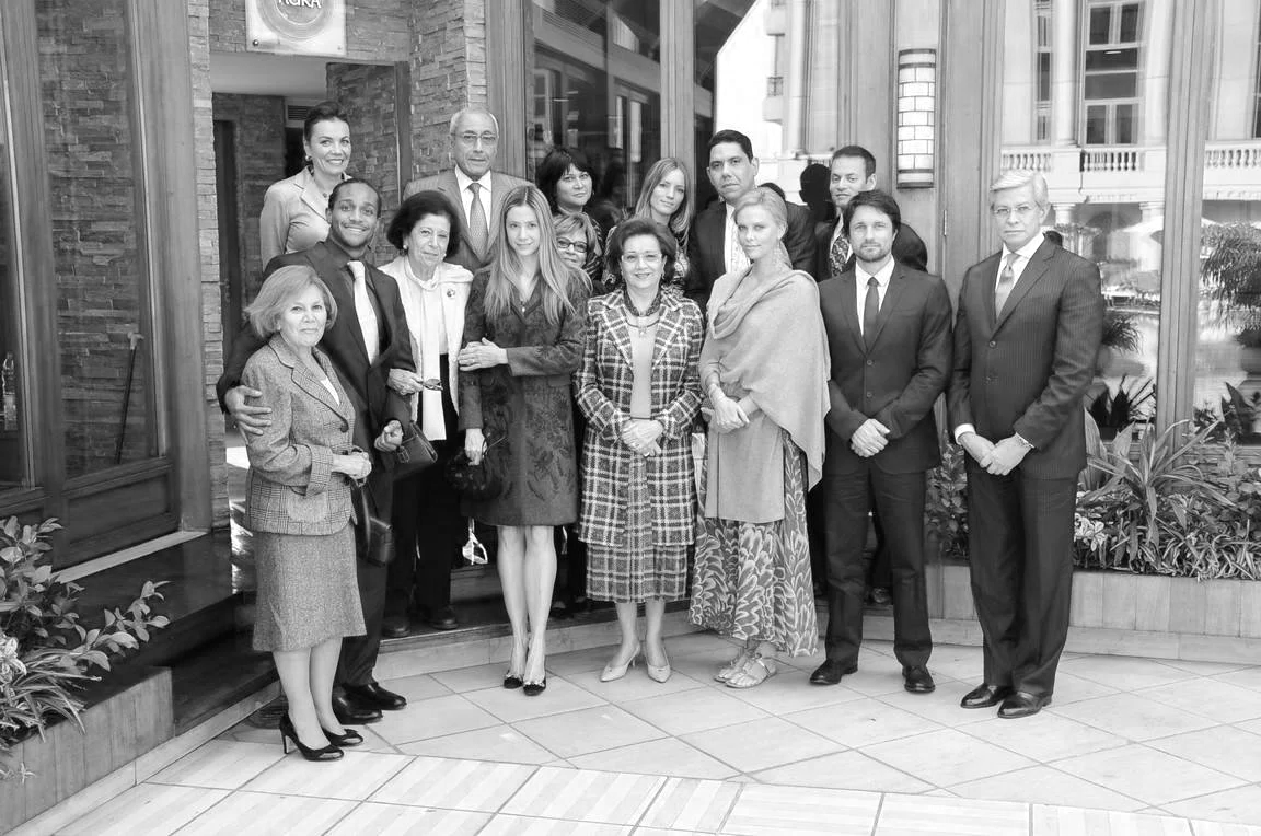 A group of diverse men and women dressed in formal attire posing for a photo outside a building with large windows.