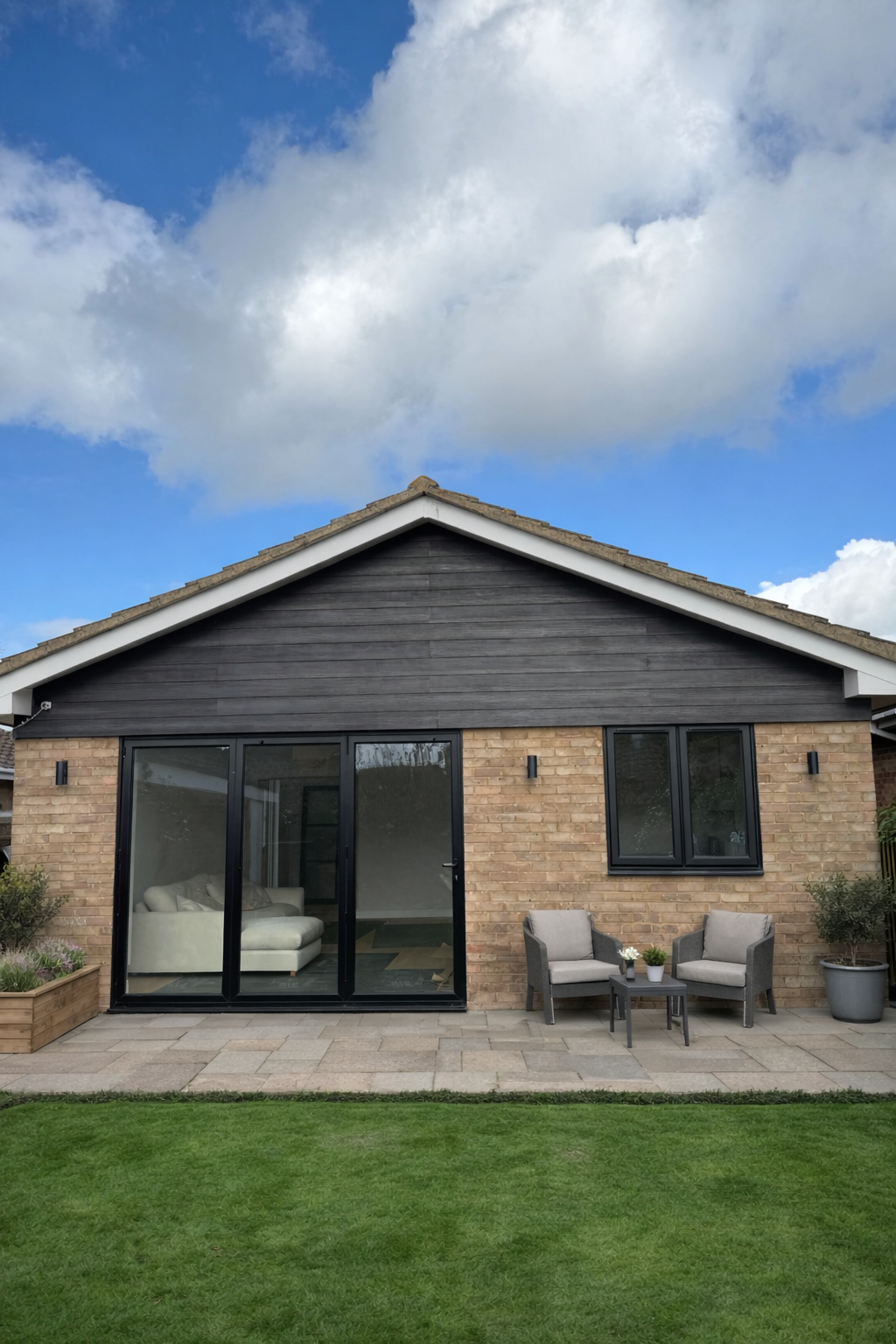 A view of a modern brick bungalow with brand new black cladding installed by Earls Construction above large glass sliding doors.