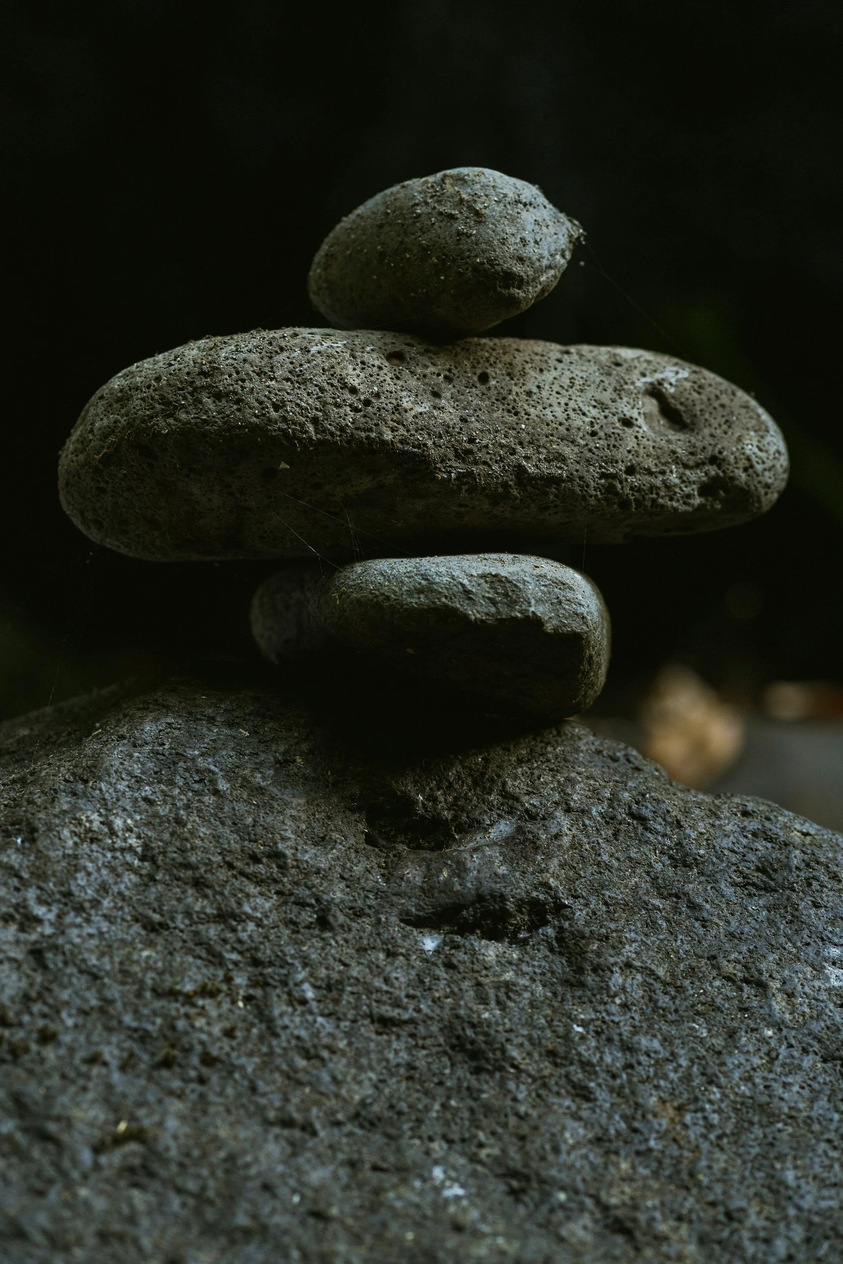 A stack of five dark, textured stones balanced on each other against a dark background
