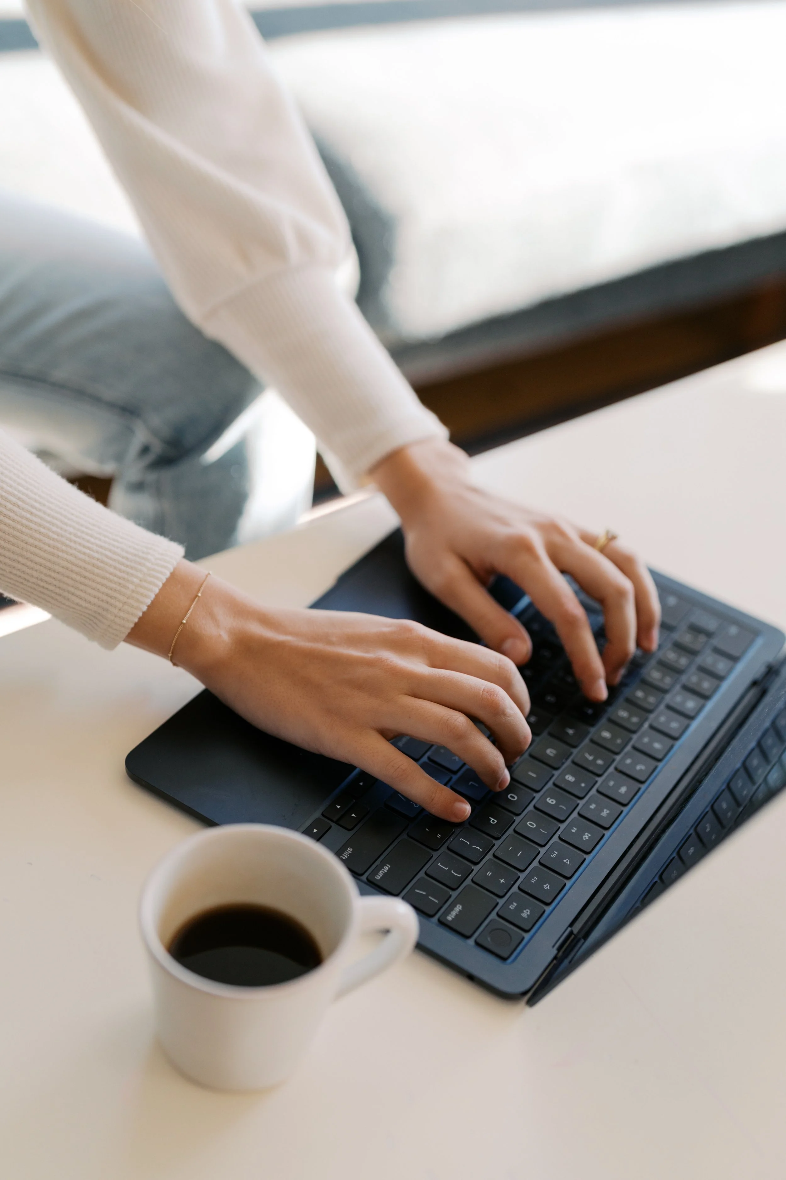 Person typing on a compact keyboard with a cup of coffee nearby.