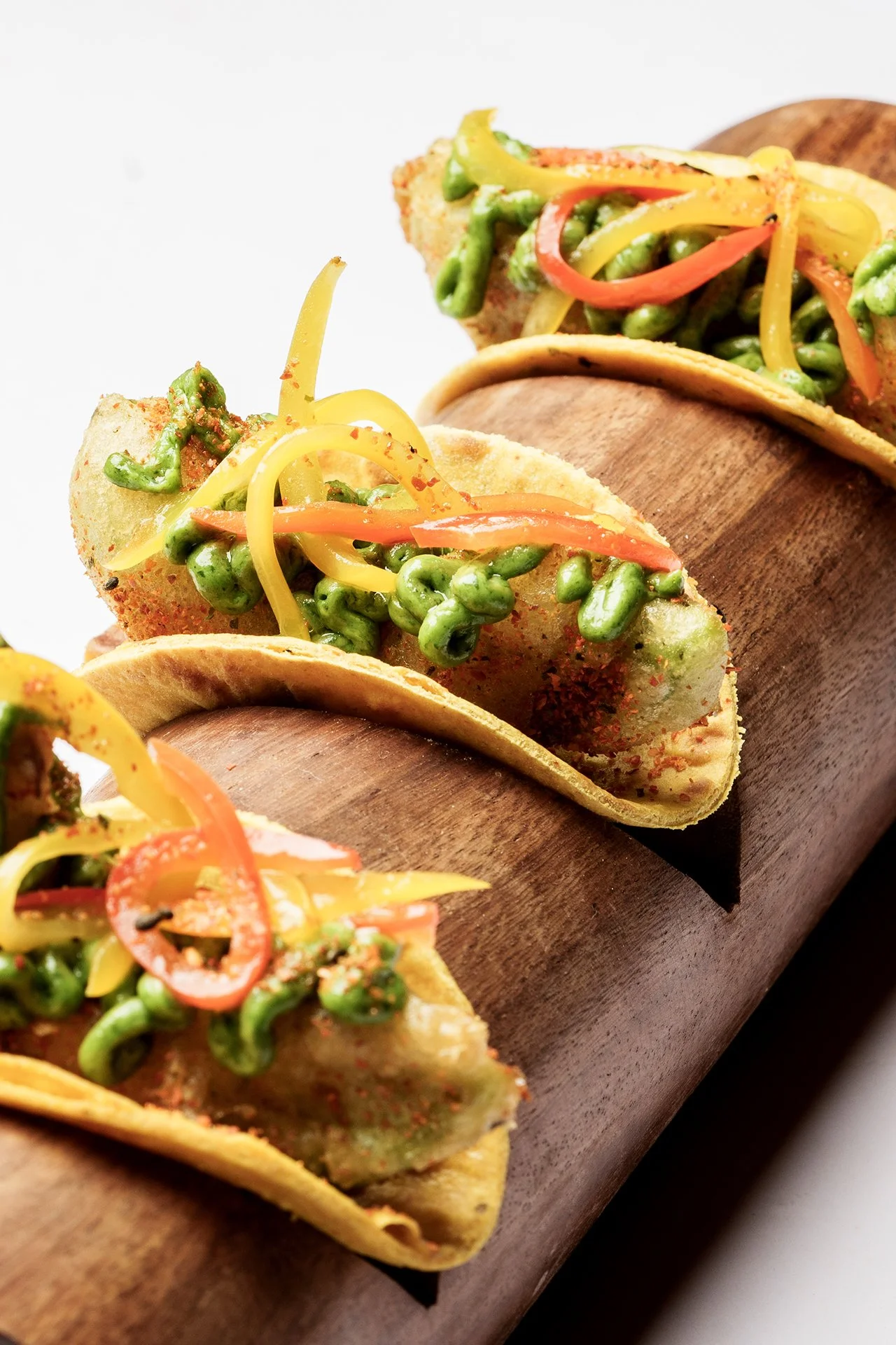 Three fish tacos with grilled fish, colorful bell peppers, and green beans inside corn tortillas on a wooden serving board.