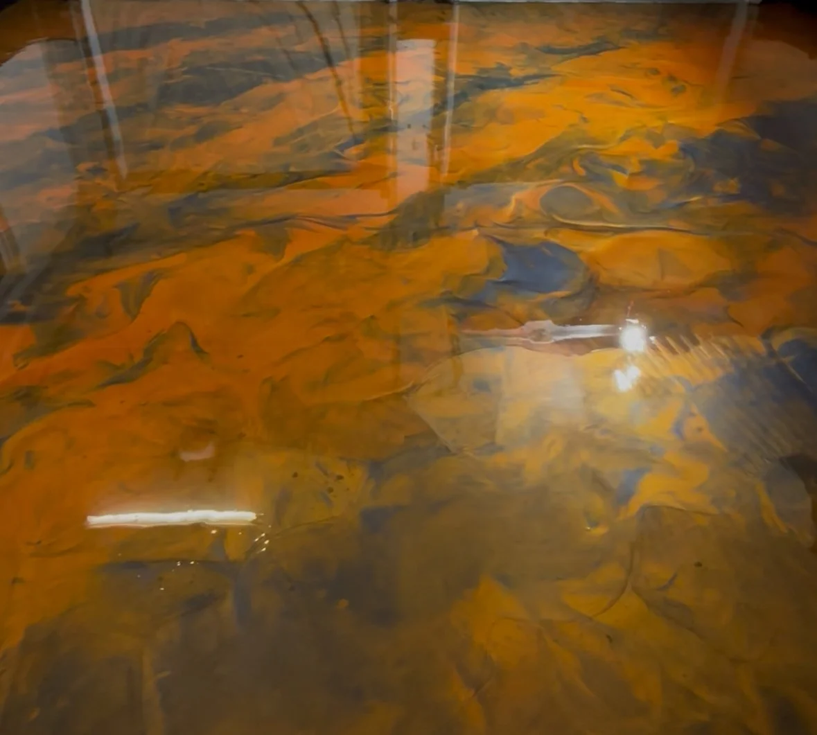 Close-up of a polished wooden surface with a rich, swirling grain pattern in shades of orange, brown, and black.