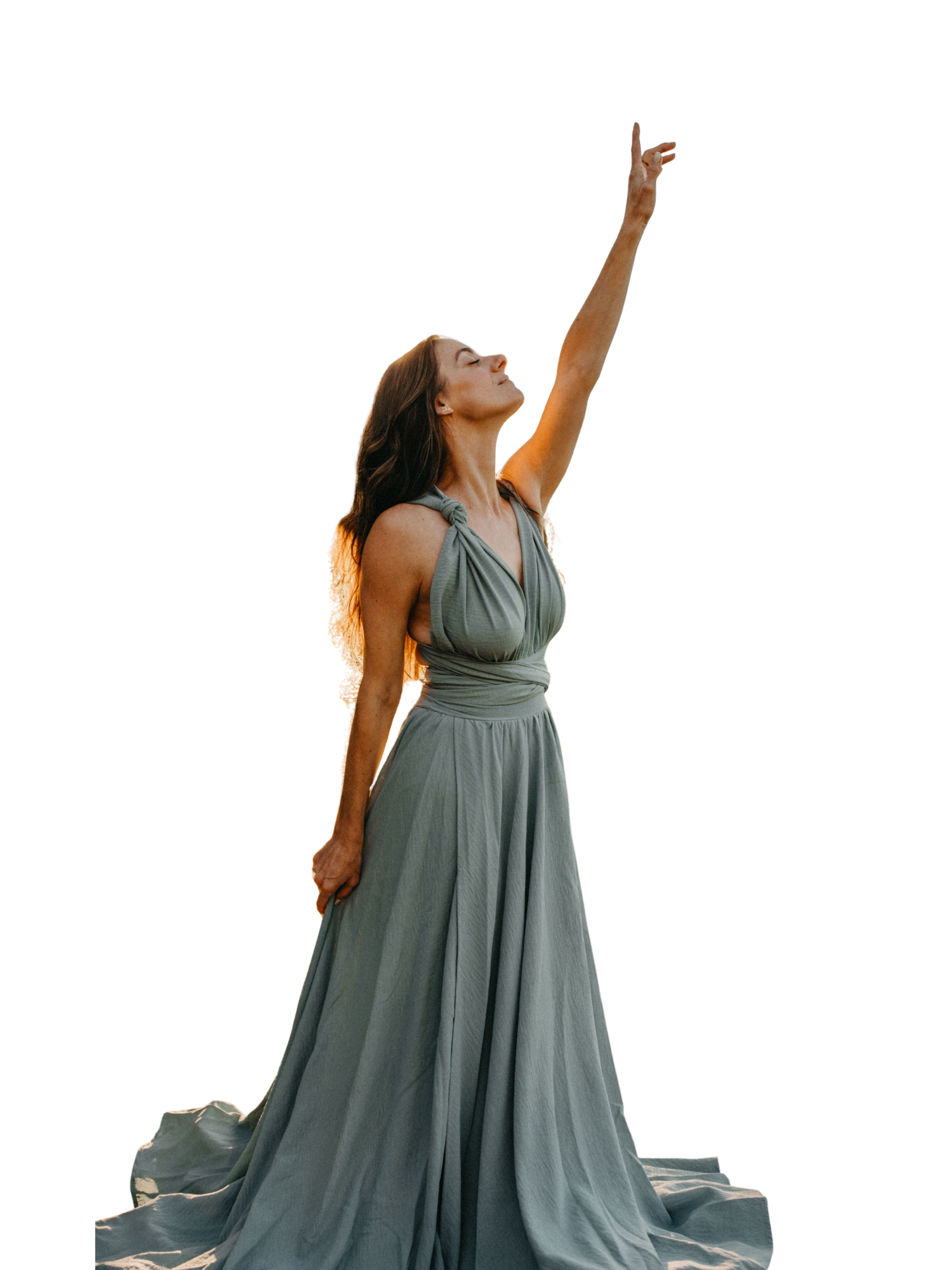 Woman in a flowing gray dress stretching her arm upward and smiling, standing against a black background.