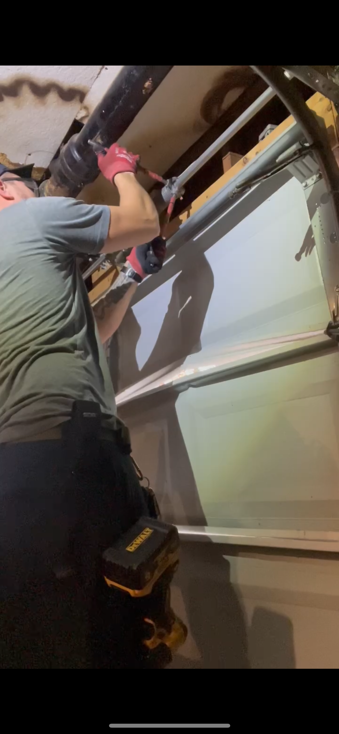 A person installing or repairing a garage door, using a cordless drill, in a garage or workshop.