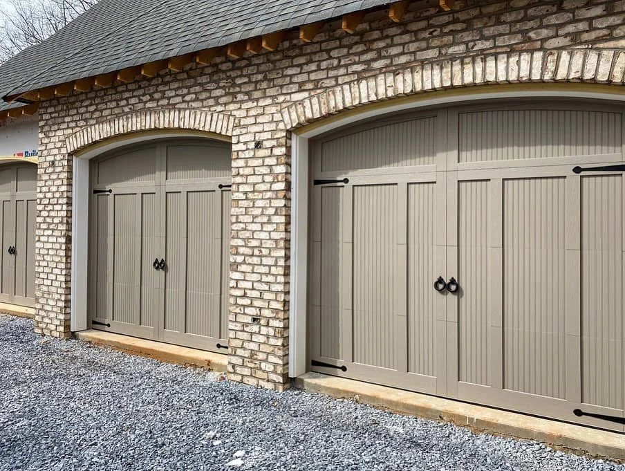 A building with white brick walls and gray garage doors with black handles and hinges.