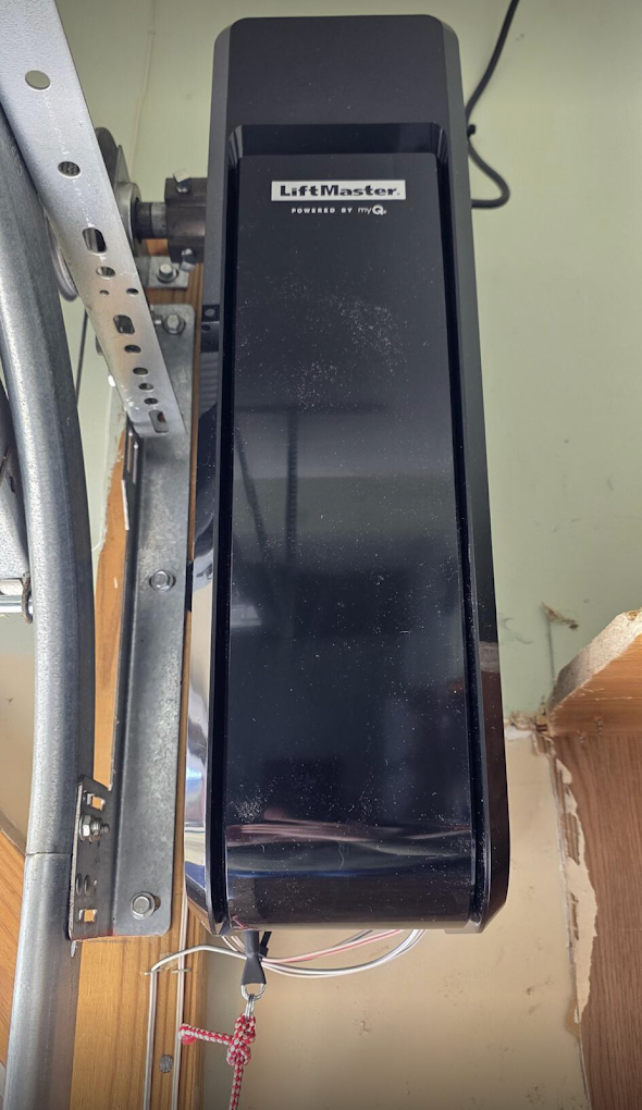 A LiftMaster garage door opener mounted on the ceiling with some dust and a power cord attached.