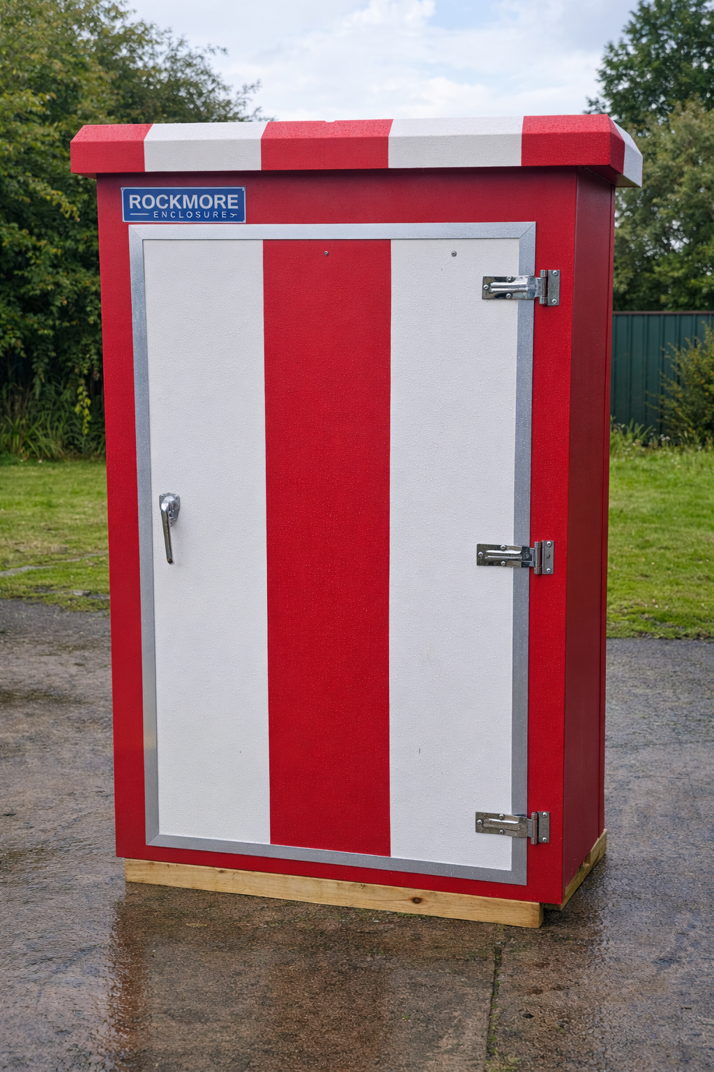 Red and white striped outdoor electrical enclosure with a lock, situated on a paved surface with grass and trees in the background.