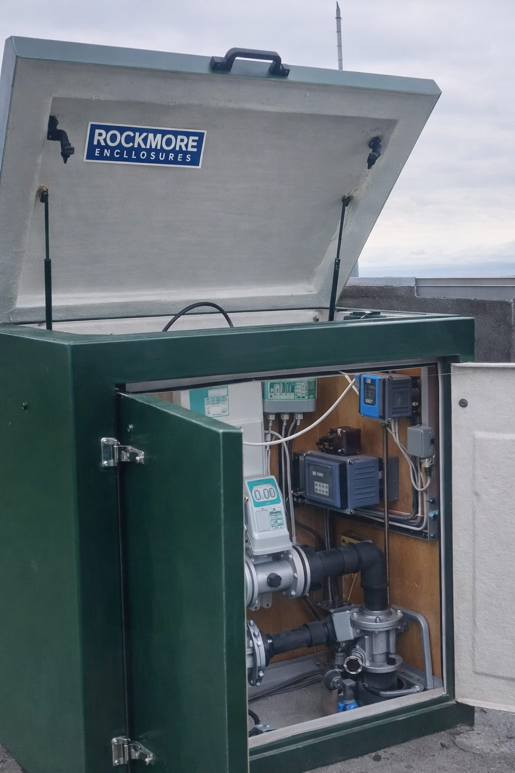 Open utility box on a rooftop containing electrical and plumbing components, with a partially visible 