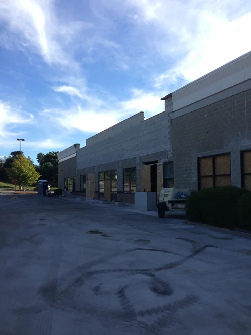 An empty parking lot in front of a storefront building under a partly cloudy sky.