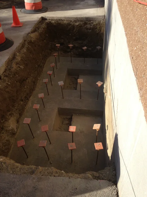 Construction site with an excavation pit and multiple small metal plates with labels on support sticks inside the trench.