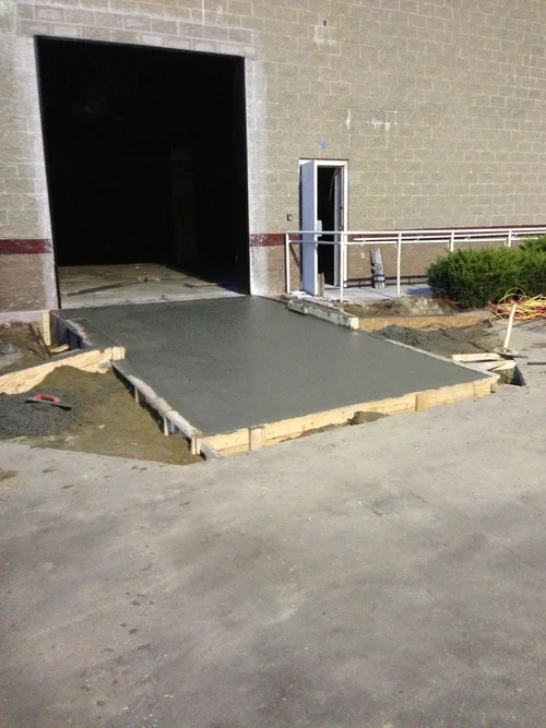 Freshly poured concrete on a building construction site, with wooden form framing, leading to a doorway.