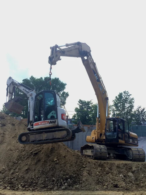 An excavator lifting a smaller excavator at a construction site.