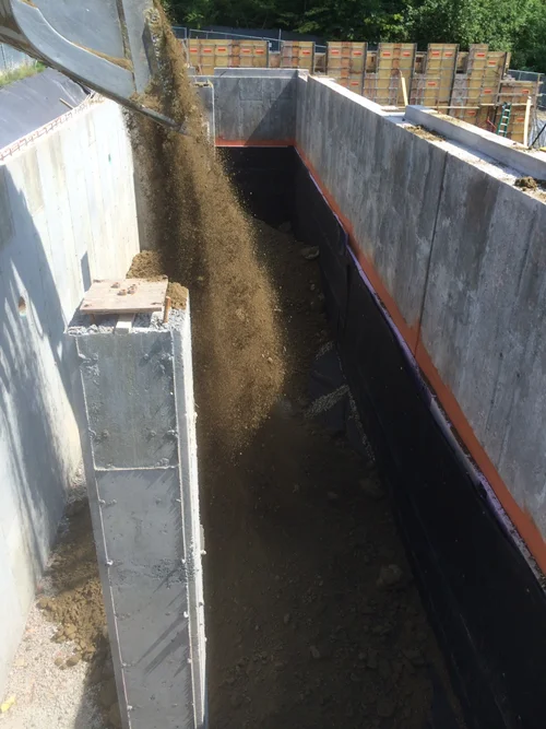 Construction site with dirt being poured into a trench from a large scoop or conveyor.