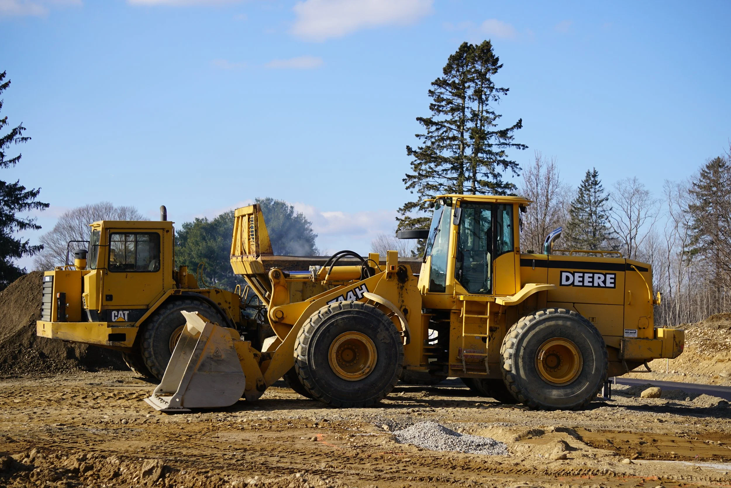 A yellow Caterpillar bulldozer on a construction site with dirt and soil, trees in the background, and a clear blue sky.