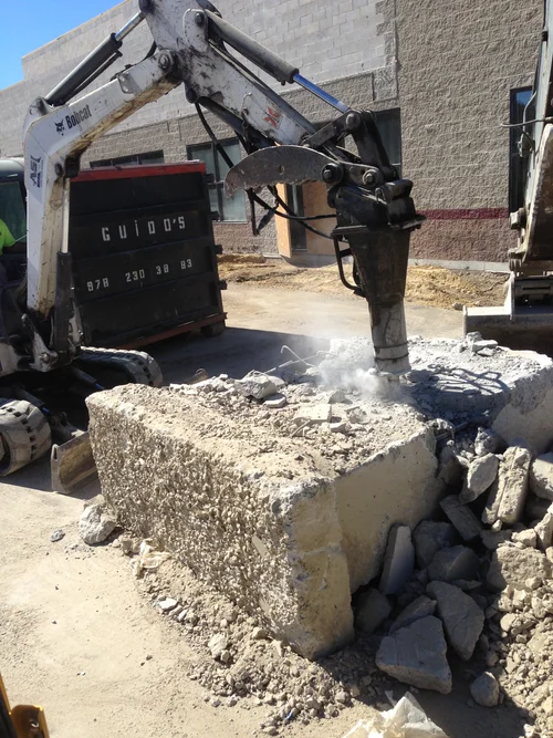 An excavator breaking a large concrete block on a construction site.