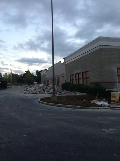 Construction site outside a building with debris and construction materials near the curb under cloudy skies.