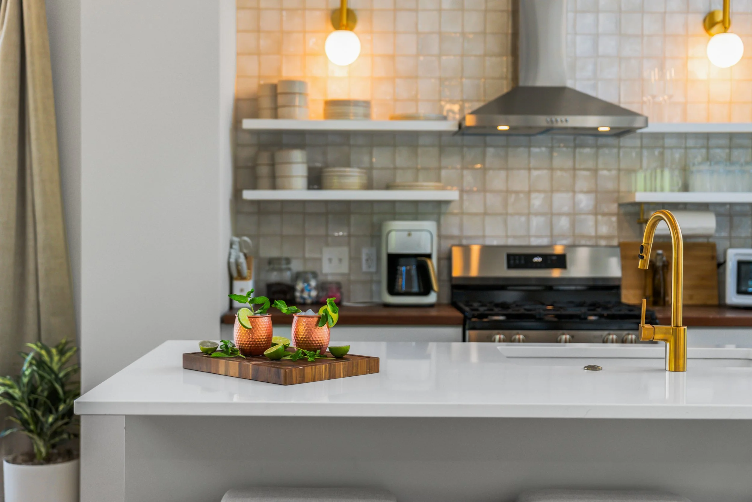 Modern kitchen with white countertop, gold faucet, stove, coffee maker, microwave, and open shelving with plates and containers