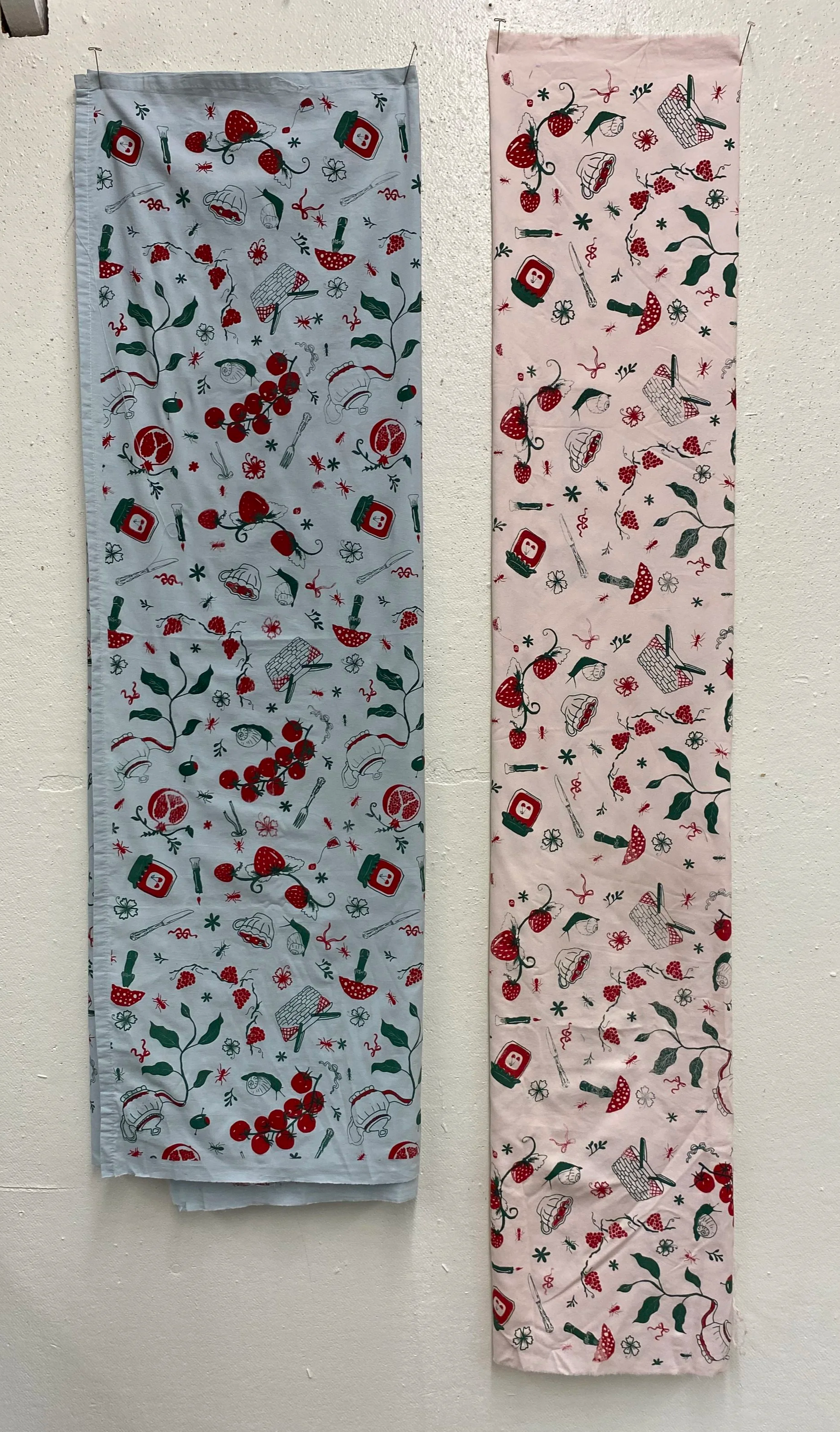 Two decorative fabric strips hanging on a wall with Christmas-themed illustrations including holly, berries, mushrooms, and jars of jam.