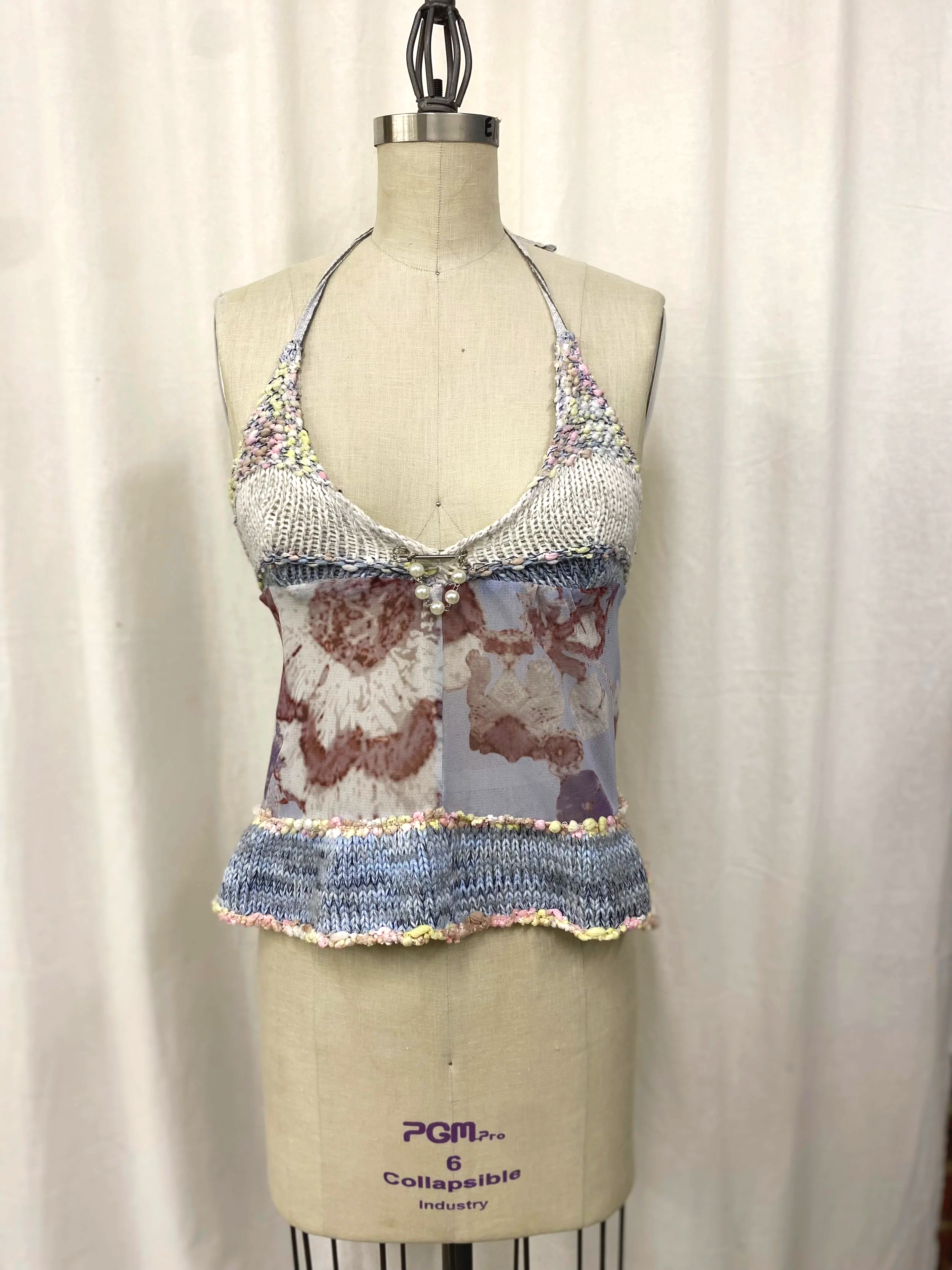 A dress form displaying a patchwork sleeveless top with a floral pattern and decorative pearl accents, seen against a plain background.