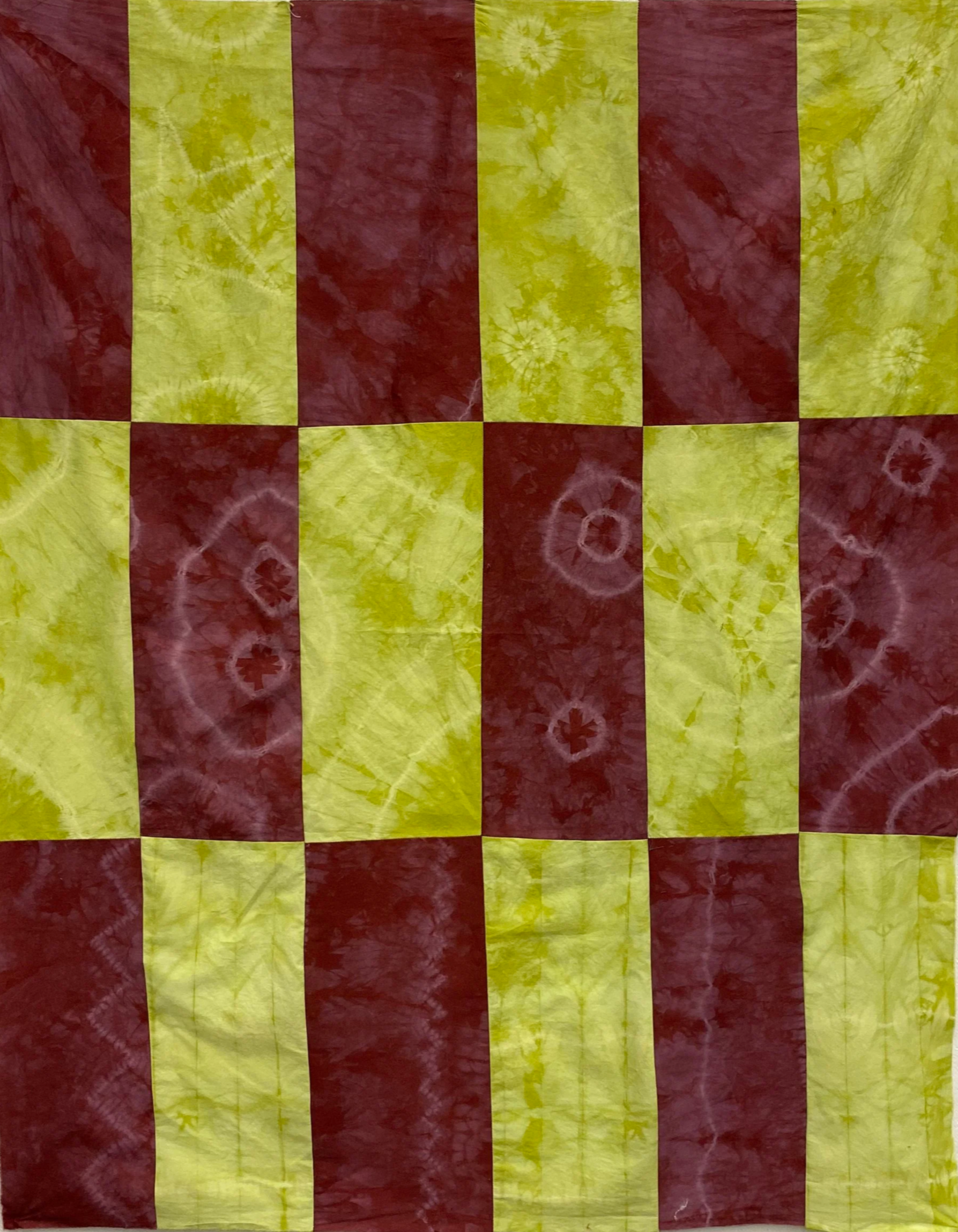 A colorful patchwork fabric with alternating red and yellow-green tie-dye squares arranged in a checkered pattern.