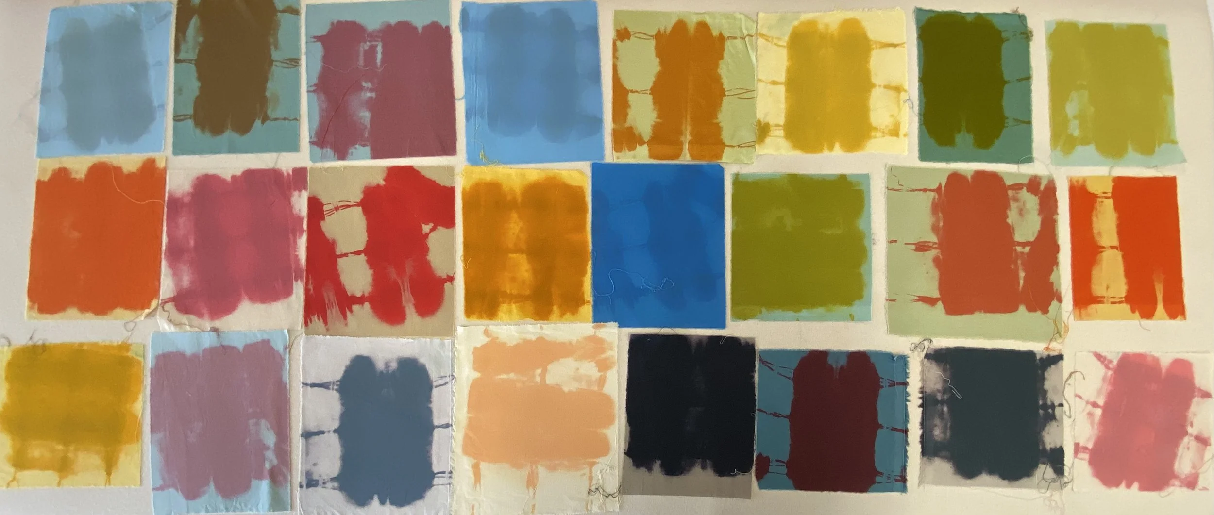 Collection of watercolor fabric swatches in various colors including blue, pink, yellow, green, orange, black, and peach, arranged on a surface.