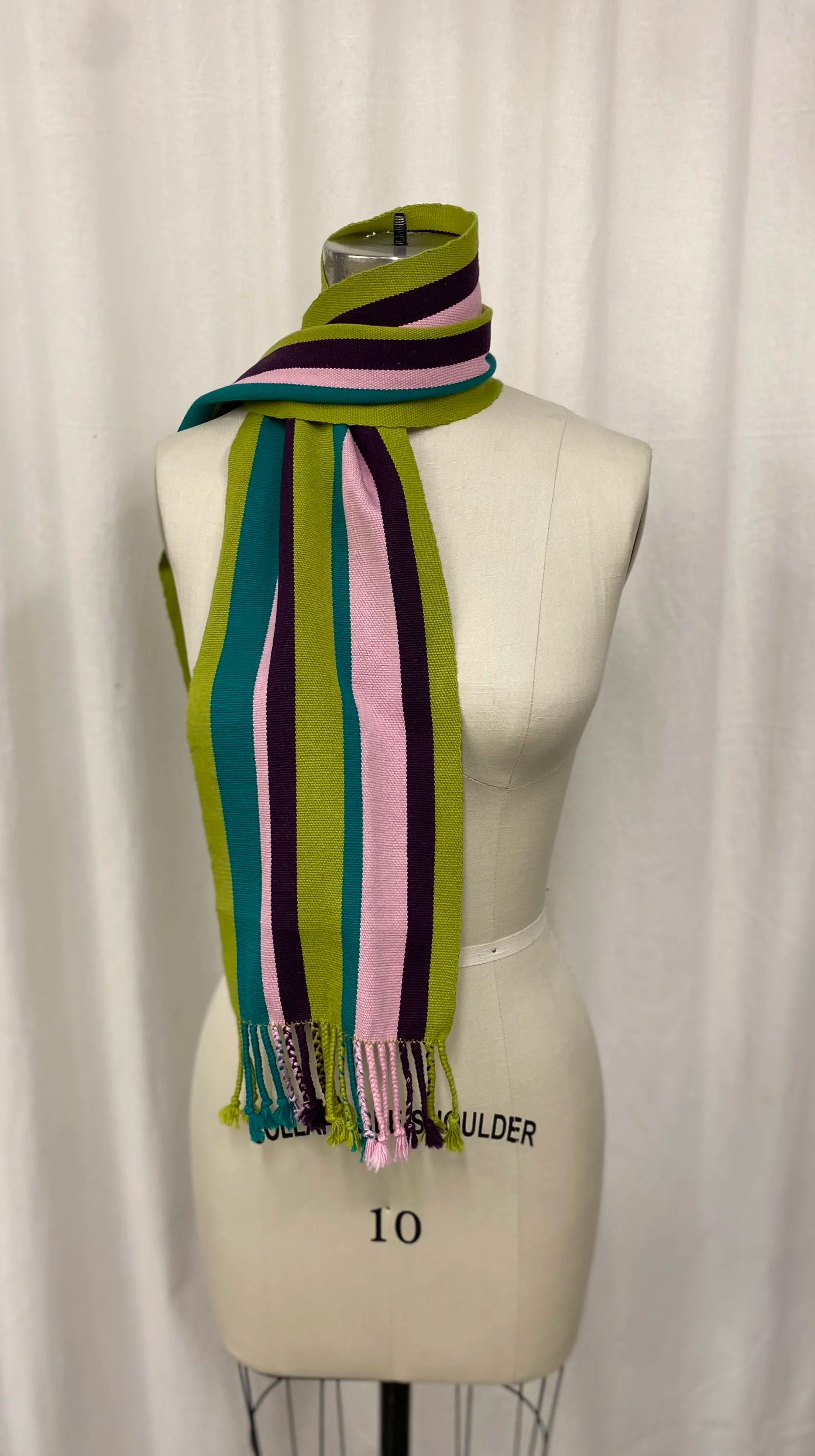 Colorful striped scarf with green, black, pink, and teal stripes draped around a dress form on a white background.