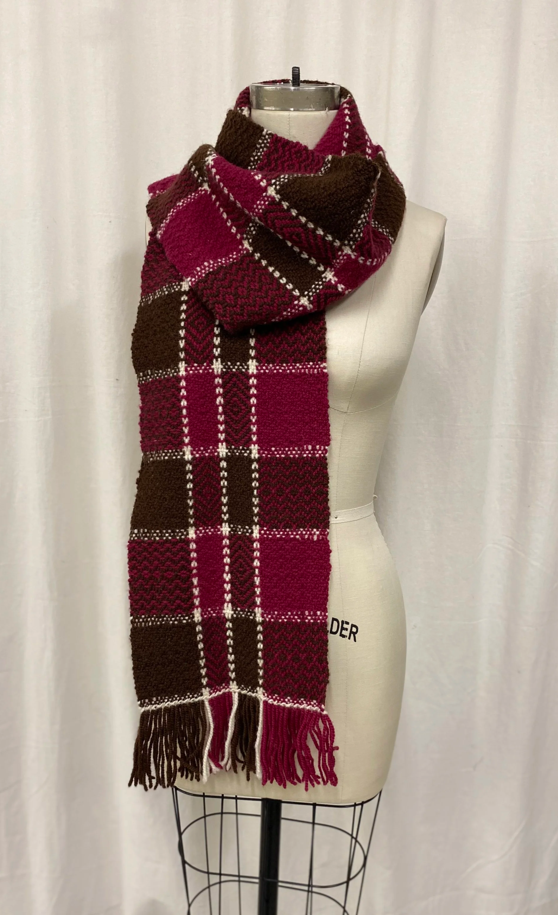 Mannequin wearing a plaid scarf in shades of red and brown with white accents, draped around the neck.