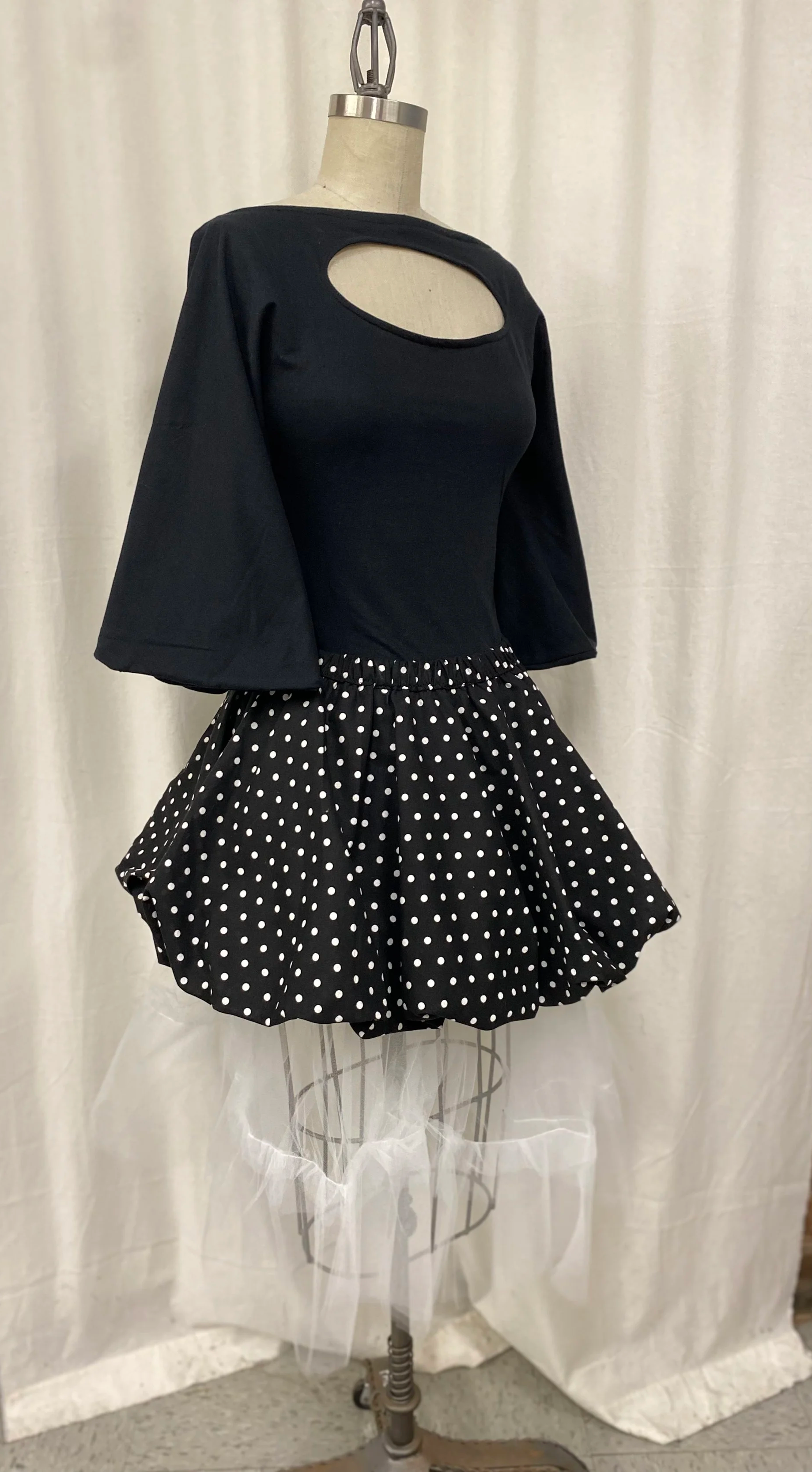 Black top with a cutout at the shoulder, paired with a black and white polka dot skirt with ruffles.