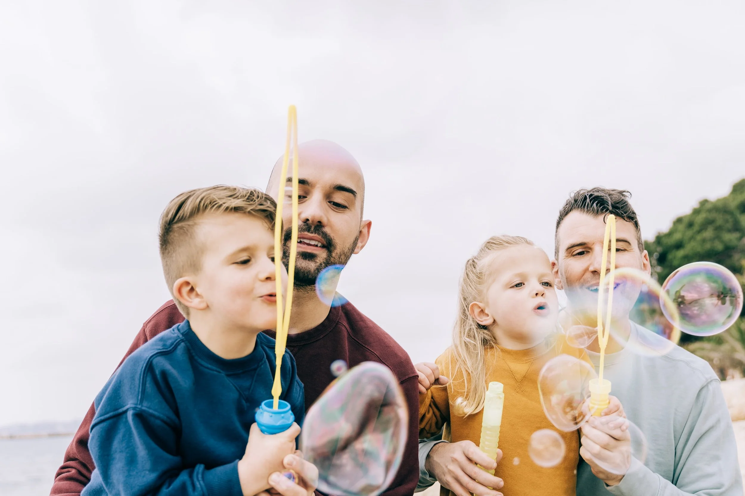 Group of children and adults outdoors blowing bubbles on a cloudy day, happy from caregiver coaching from a BCBA.