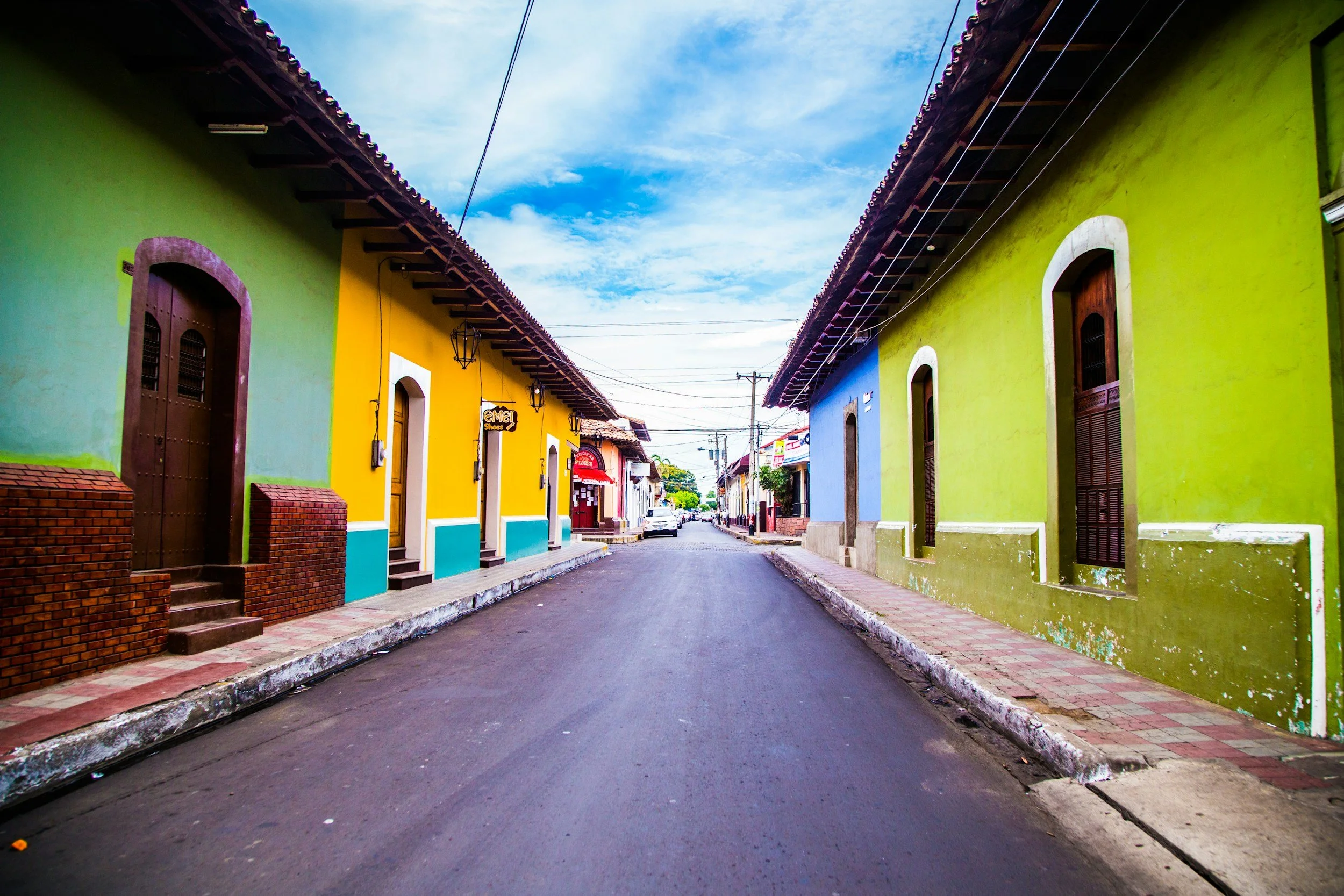 A colorful street with bright green and yellow buildings, a clear blue sky, and a close-up view showing houses with wooden doors and small steps leading to the entrances.