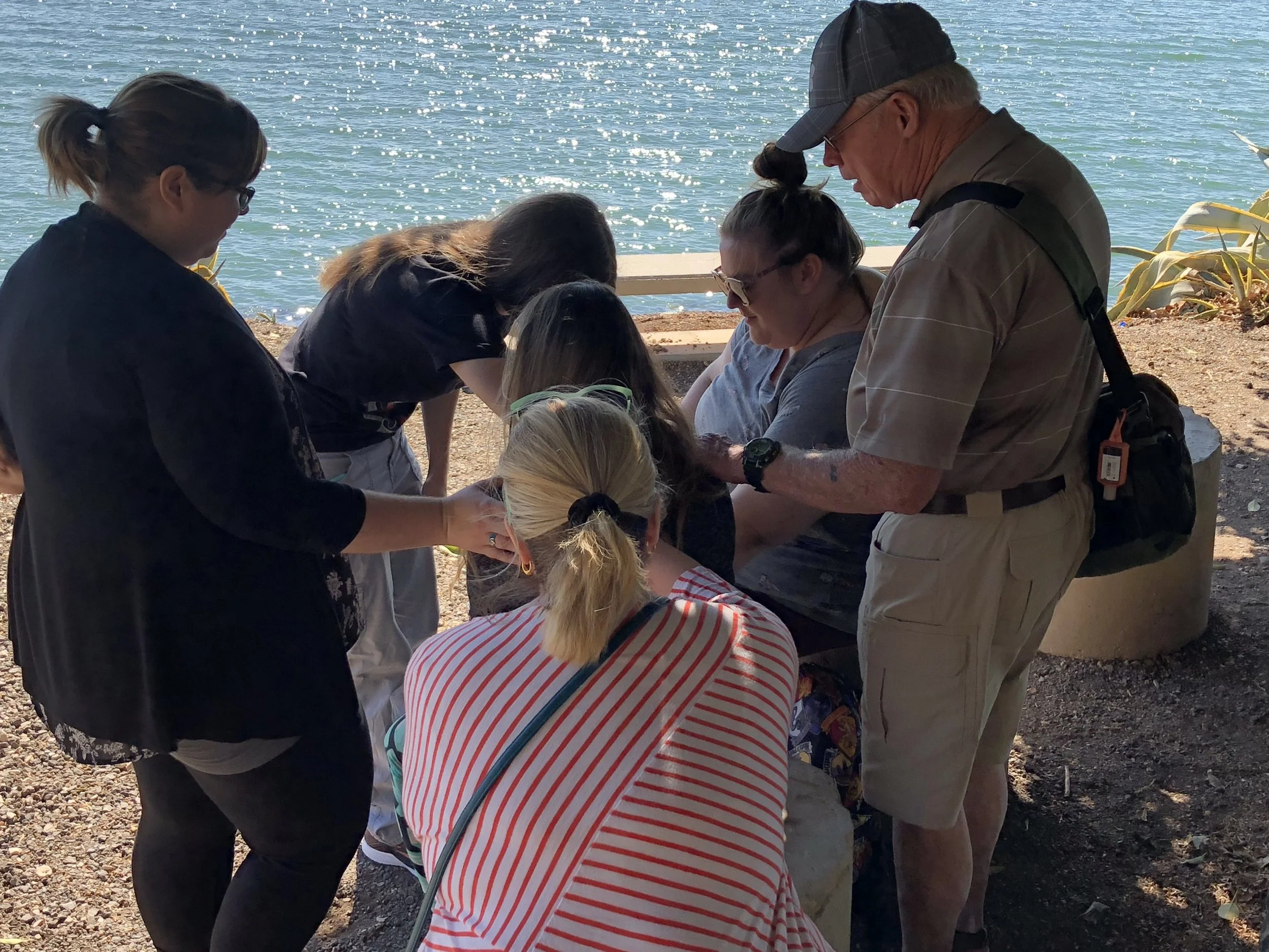 Group of people gathered closely together outdoors by the water on a sunny day.